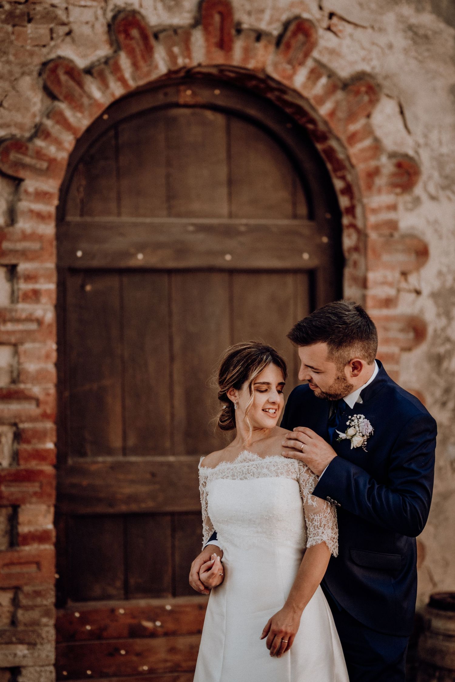 Bride and groom sharing an intimate moment before a rustic arched wooden door with ornate brick frame.