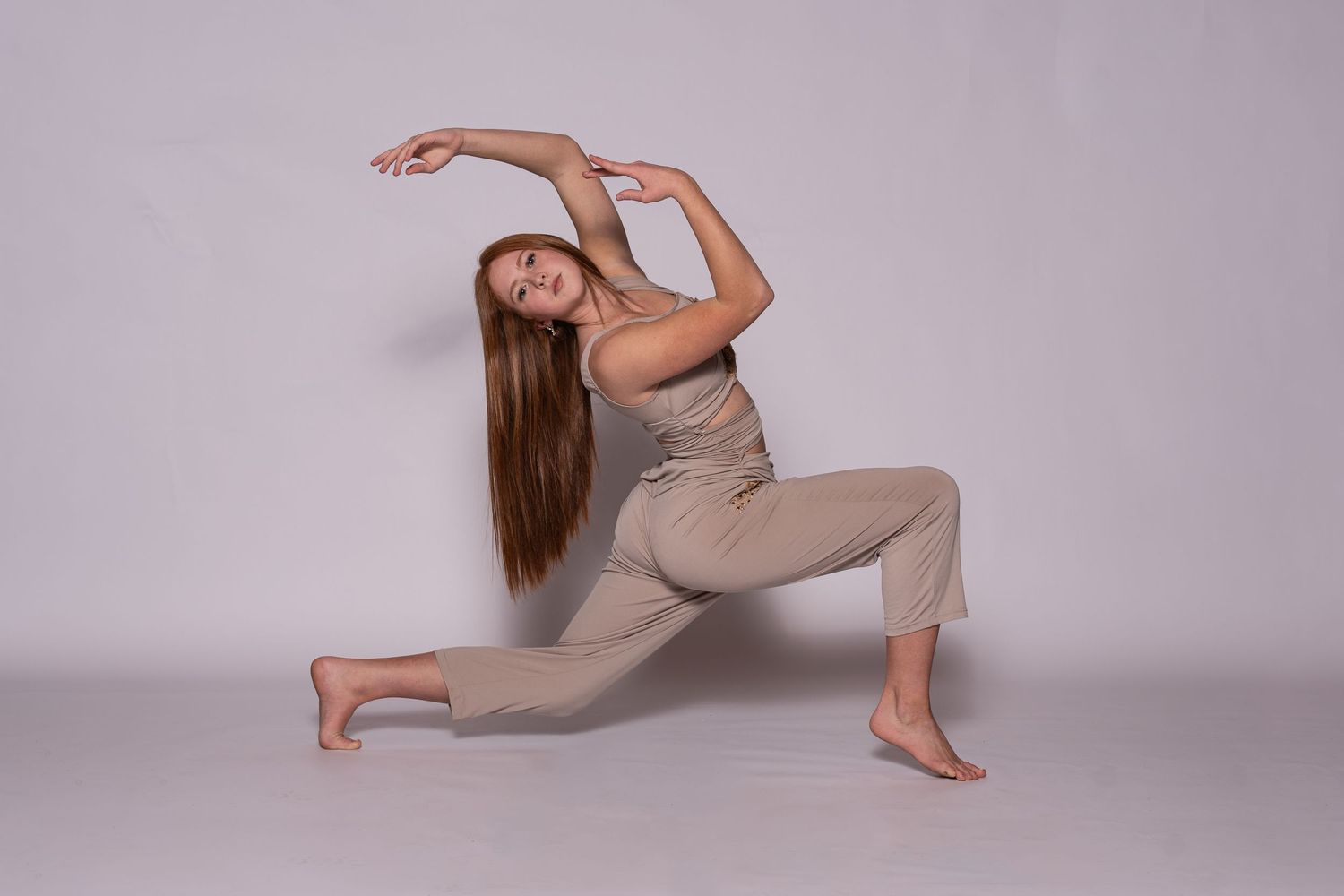 A dancer in a beige bodysuit performs contemporary dance movements on a light gray backdrop.