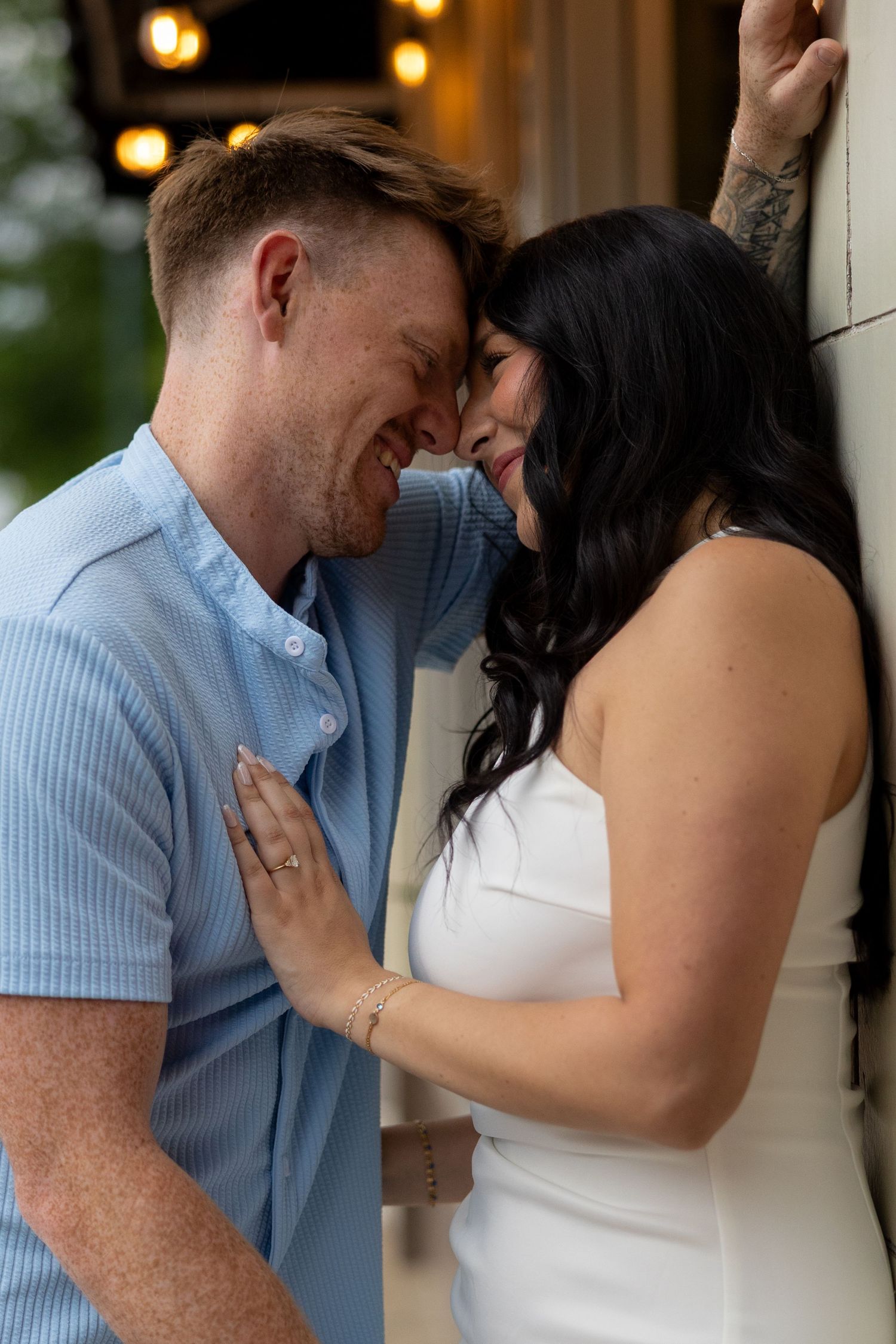 A romantic couple shares an intimate moment together against a wall with soft lighting in the background.