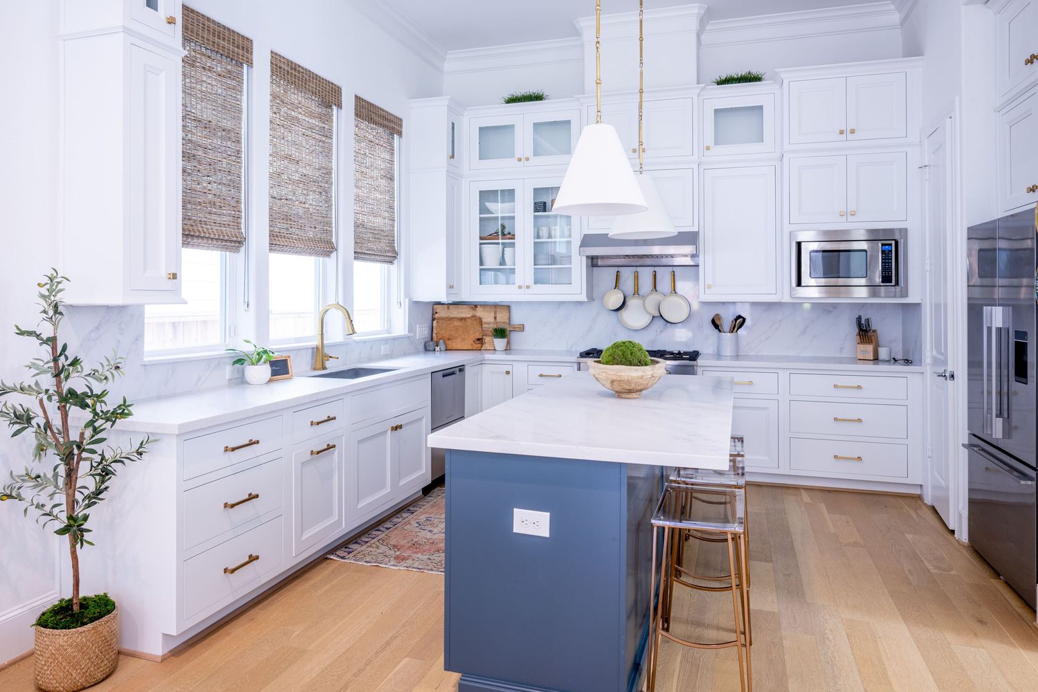 Modern white kitchen with wood floors, two-tone cabinets, and stainless steel appliances features a long waterfall island.