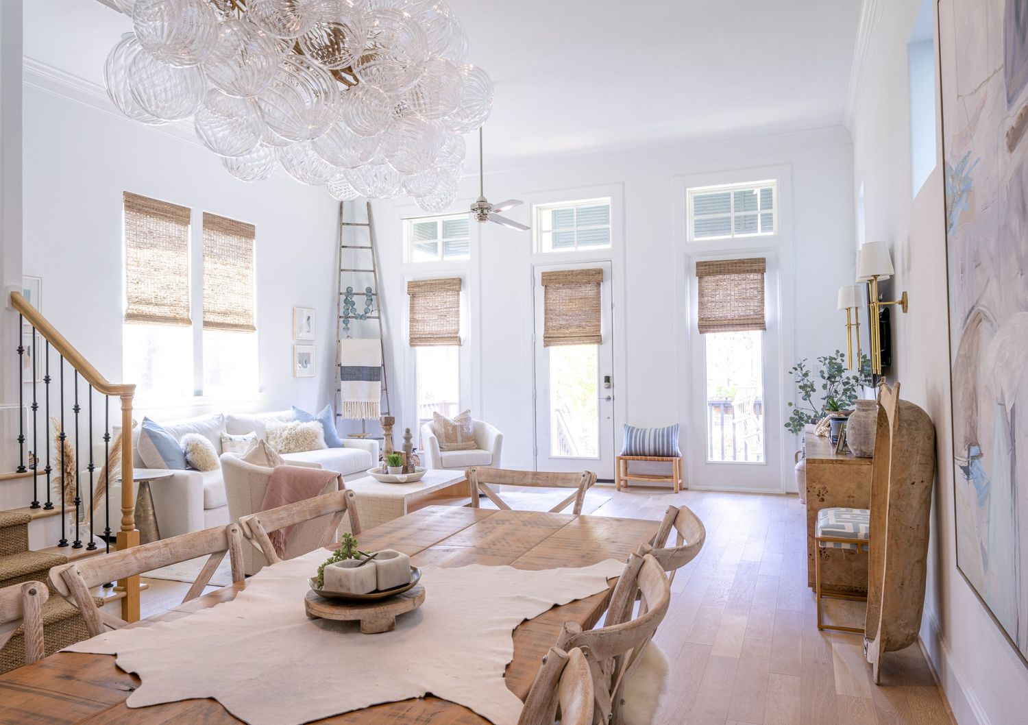 Elegant coastal living room with high ceilings features bamboo shades, neutral decor, and a luxurious crystal chandelier.