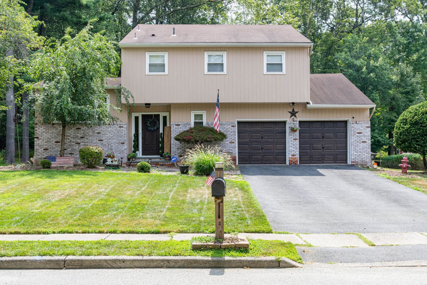Beige and stone two-story suburban house with attached two-car garage, hanging flower baskets and landscaped front yard.