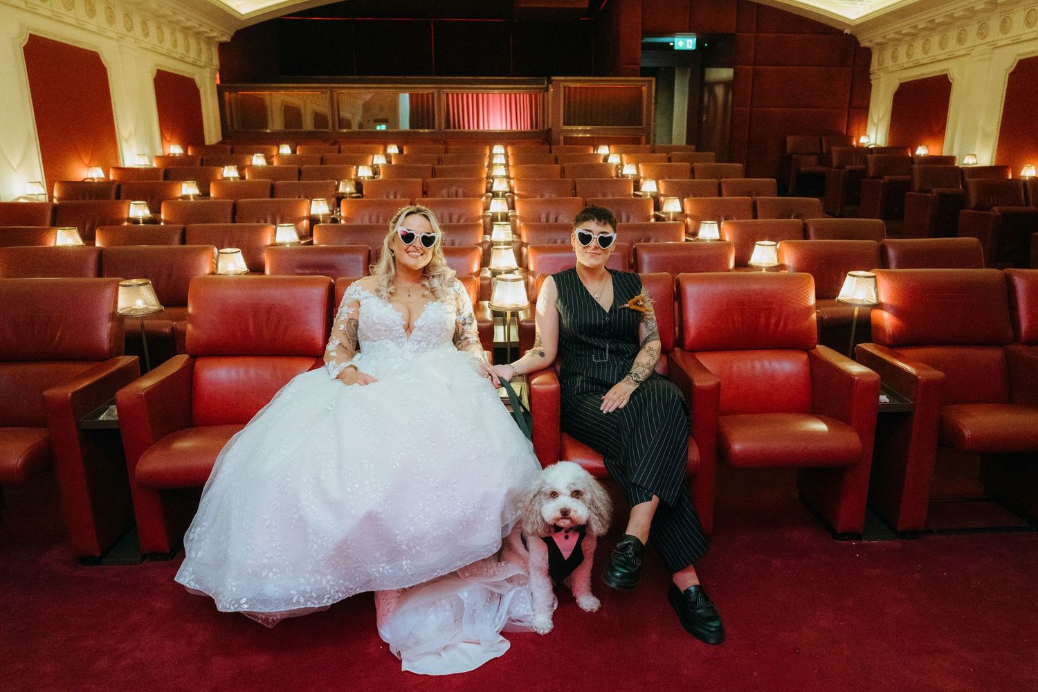 A wedding couple and their dog pose on red carpeted theater stairs in a series of elegant photos.