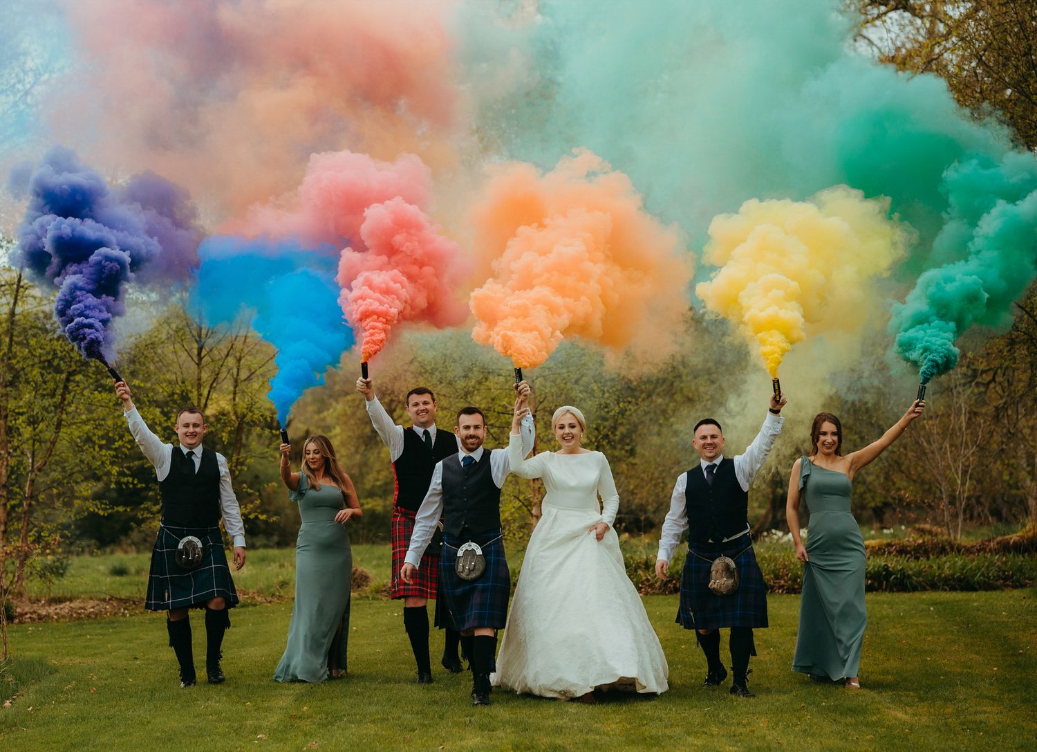 Wedding party holding colorful smoke bombs creating a rainbow effect against an autumn backdrop.