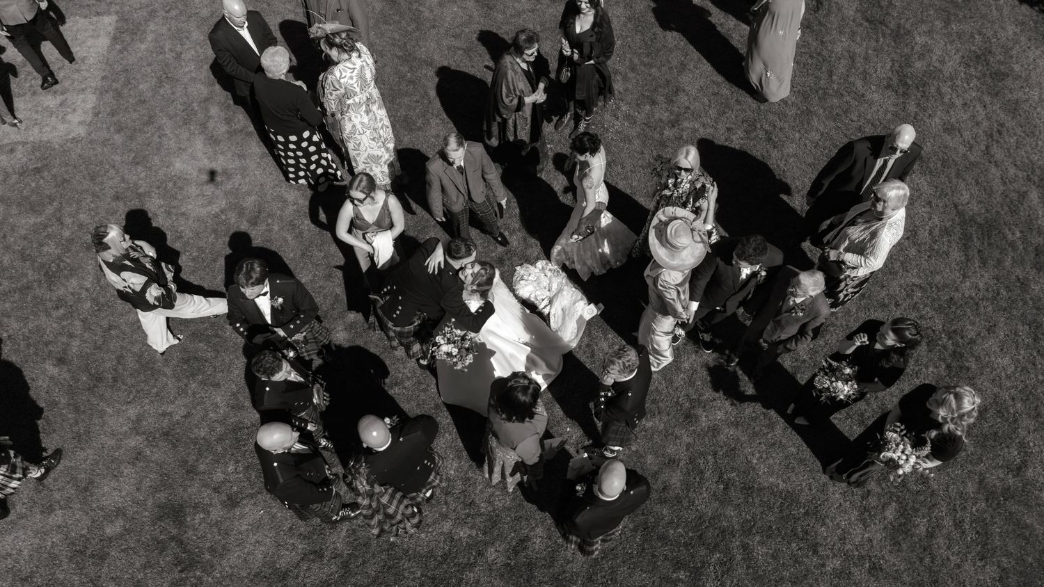 Aerial black and white photo of wedding guests mingling outdoors on grass during a reception.