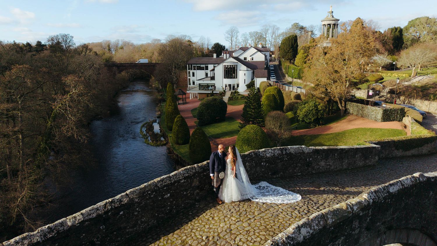Scenic riverside view of stone buildings and autumn trees along a peaceful waterway in a quaint village setting.