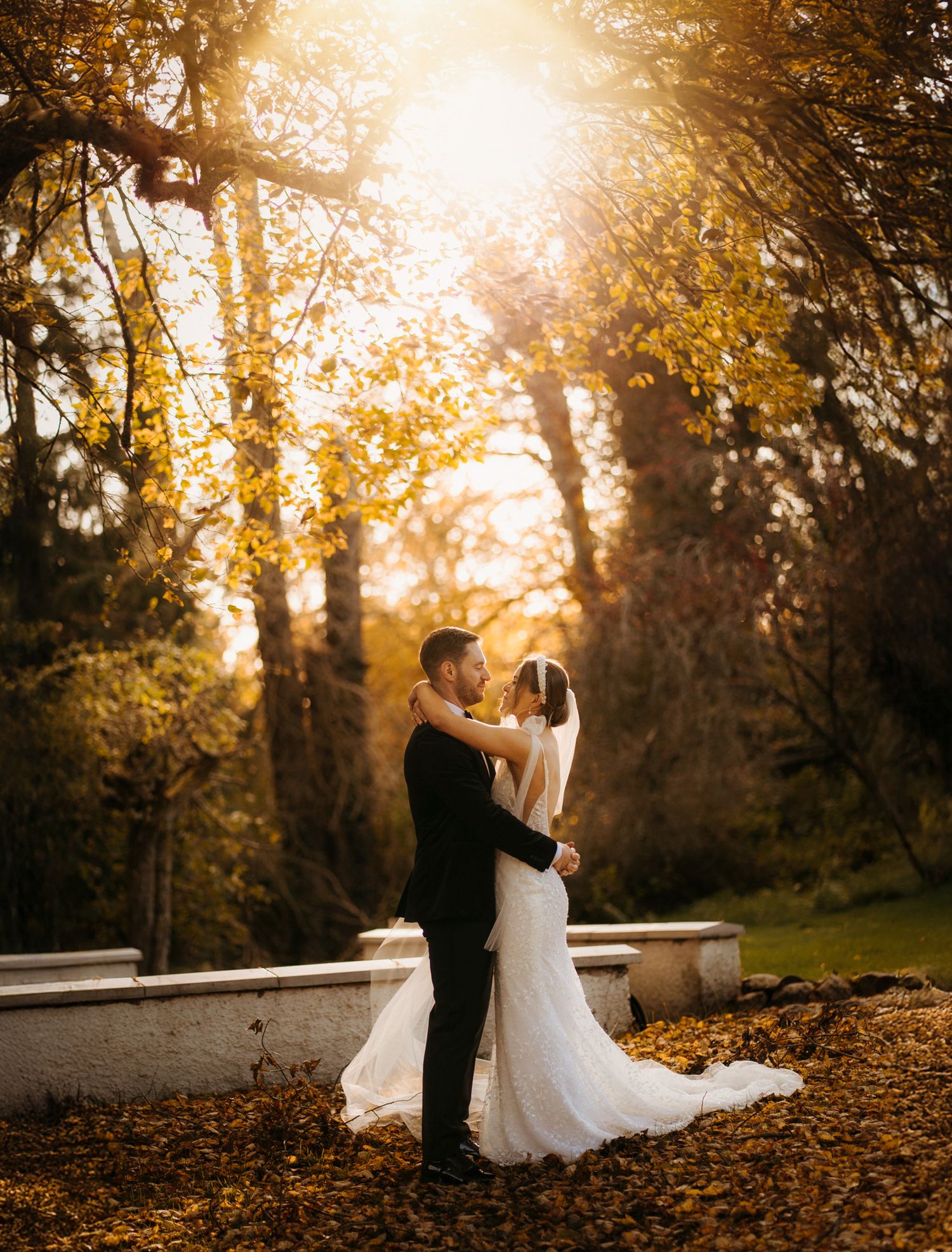 A couple dances together in a romantic autumn setting with golden sunlight filtering through trees and fallen leaves.