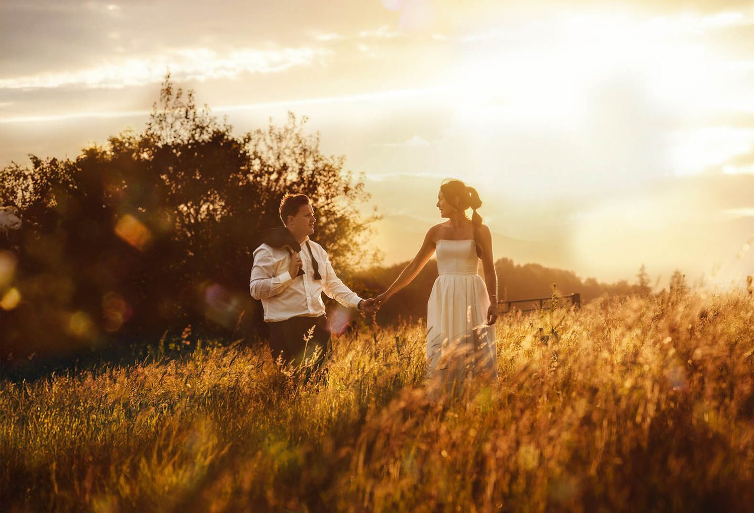 Golden sunset light illuminates a grassy field during outdoor wedding photography session.