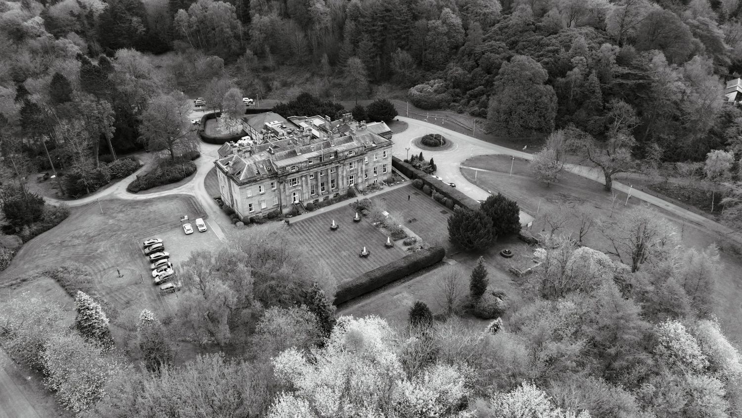 Aerial black and white view of a grand historic mansion surrounded by lush trees and manicured grounds.