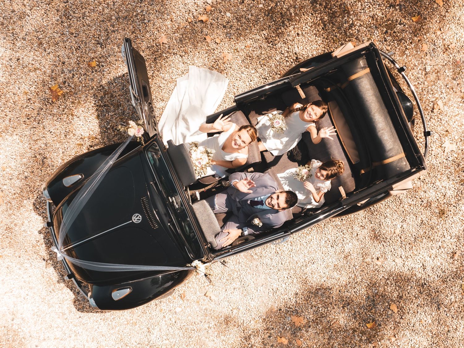 Aerial view of vintage black automobile on sandy ground with passengers visible from above.
