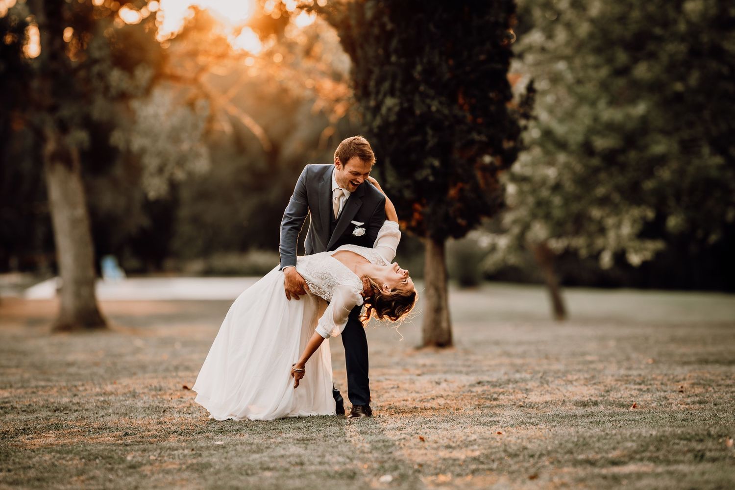 A romantic wedding couple shares intimate moments at sunset in a scenic outdoor park setting.