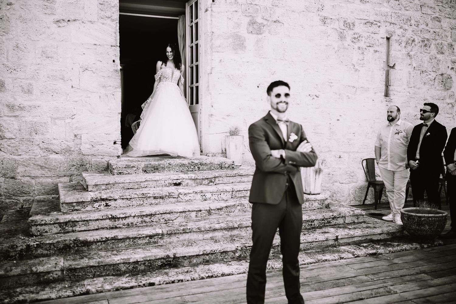 Marié souriant bras croisés devant le perron, la mariée sur le seuil de la porte, photo noir et blanc