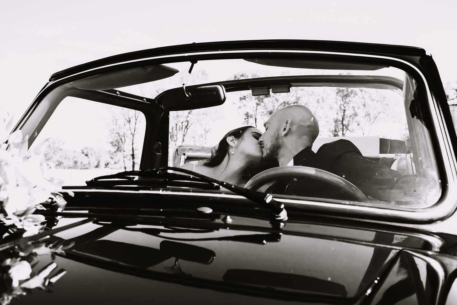 A romantic black and white photograph shows a couple sharing a tender kiss inside a vintage car.