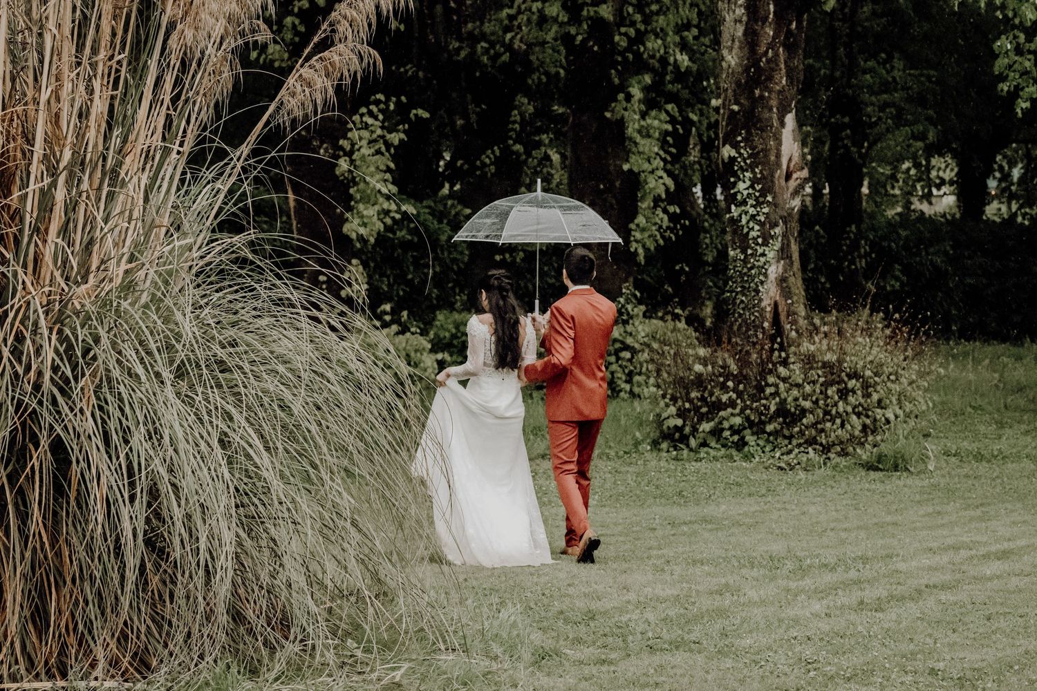 A couple walking under an umbrella in a garden during a romantic wedding photoshoot.