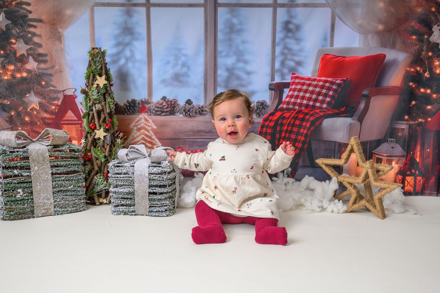 Christmas Mini Session. A small child in winter holiday attire sits on a cozy blanket with festive Christmas decorations and red stockings.