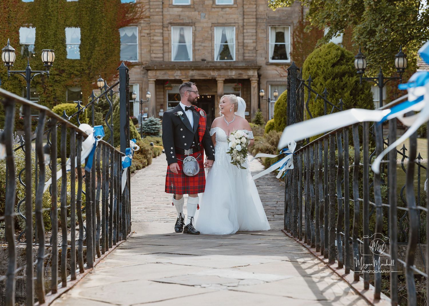 Waterton Park Hotel - A panoramic view of a wedding party walking along a bridge decorated with blue and white ribbons and flowers.
