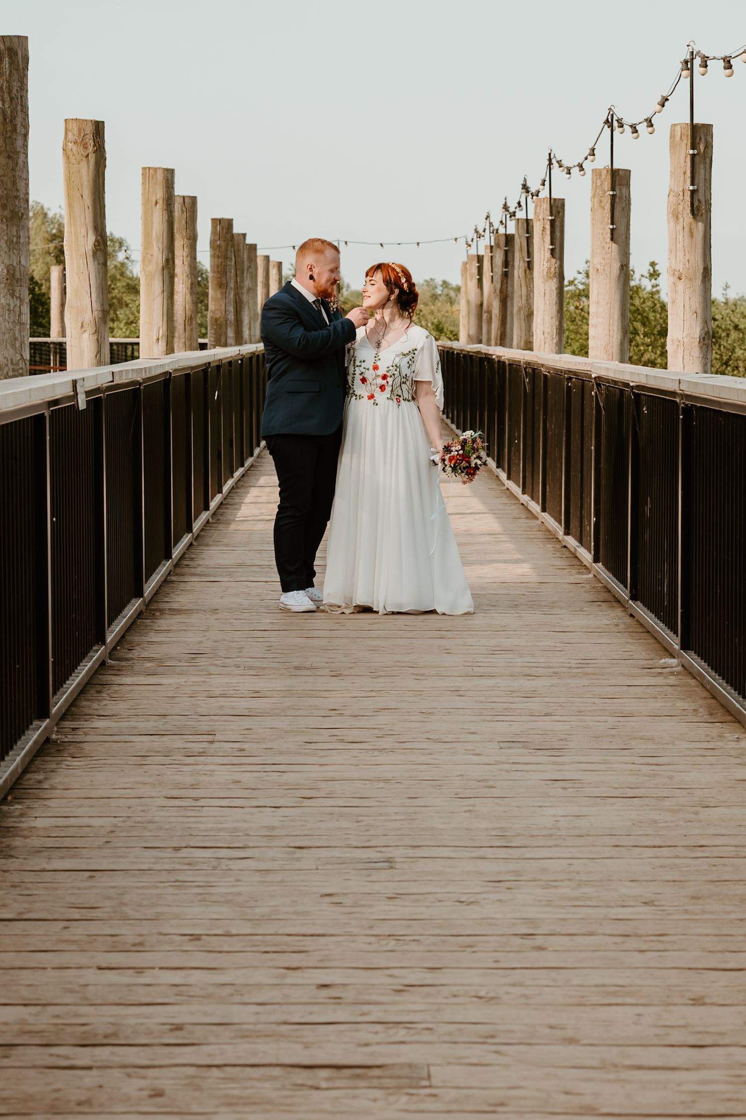 Bride and groom share a romantic moment on a wooden boardwalk lined with string lights on their wedding day.