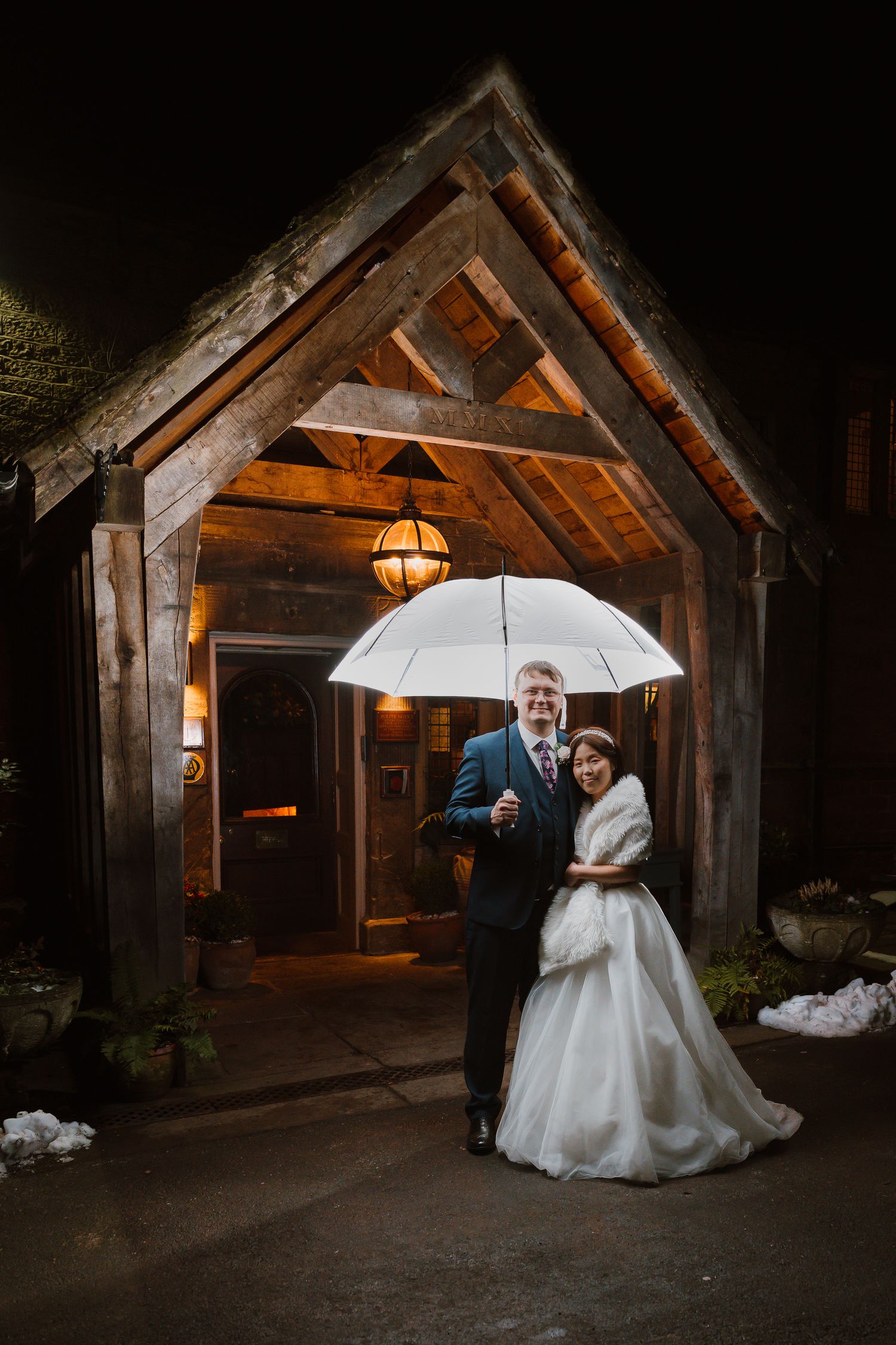 Wedding couple poses under illuminated rustic wooden gazebo, posed in front of Whitley Hall Sheffield.