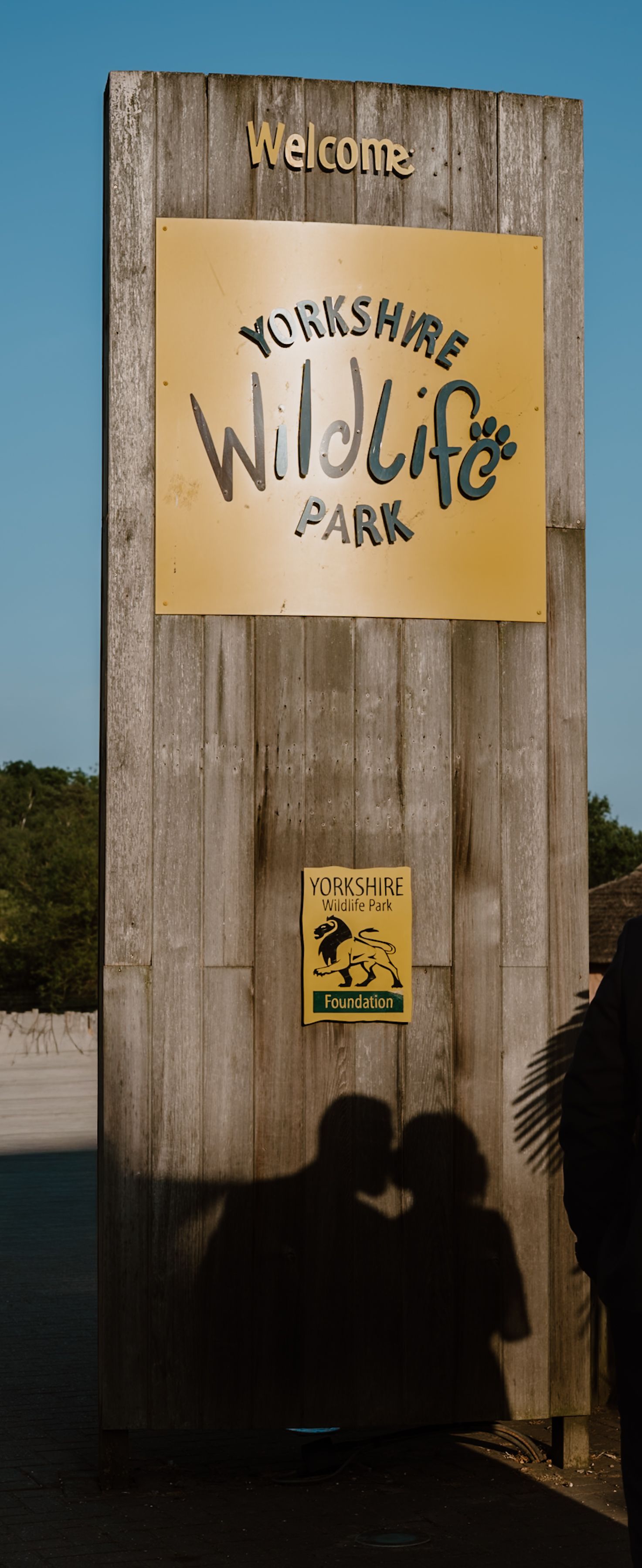 Welcome sign at Yorkshire Wildlife Park entrance with golden logo and foundation emblem on weathered wood pillar.