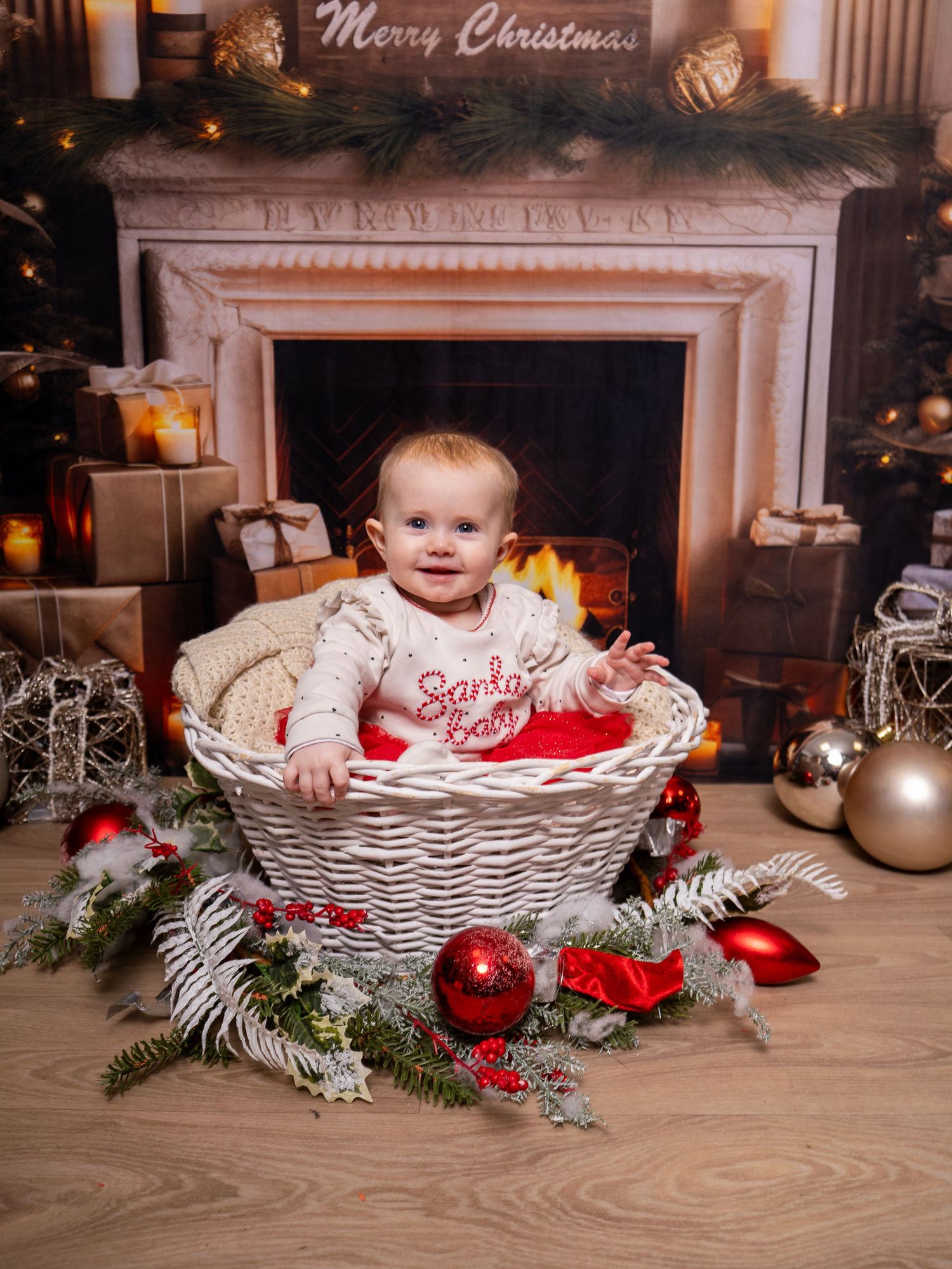 Baby sitting in white wicker basket with Christmas decorations and fireplace in background. Christmas mini session