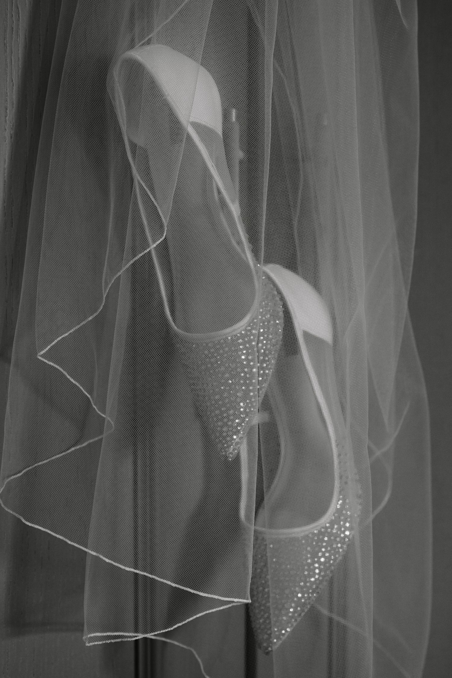 Burntwood Court Hotel. Elegant bridal shoes with crystal embellishments displayed against flowing white veil in black and white photography.
