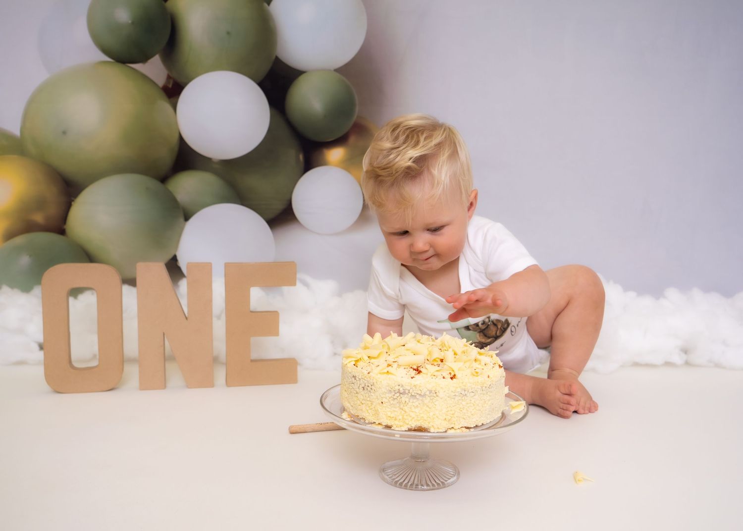 First birthday decor with olive green and white balloons against light background. Cake Smash Photoshoot