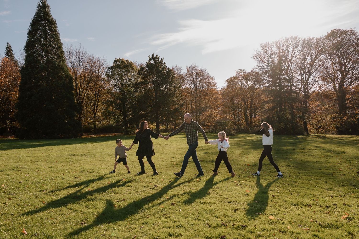 Group of people playing soccer on a grassy field on a sunny autumn day casting long shadows.