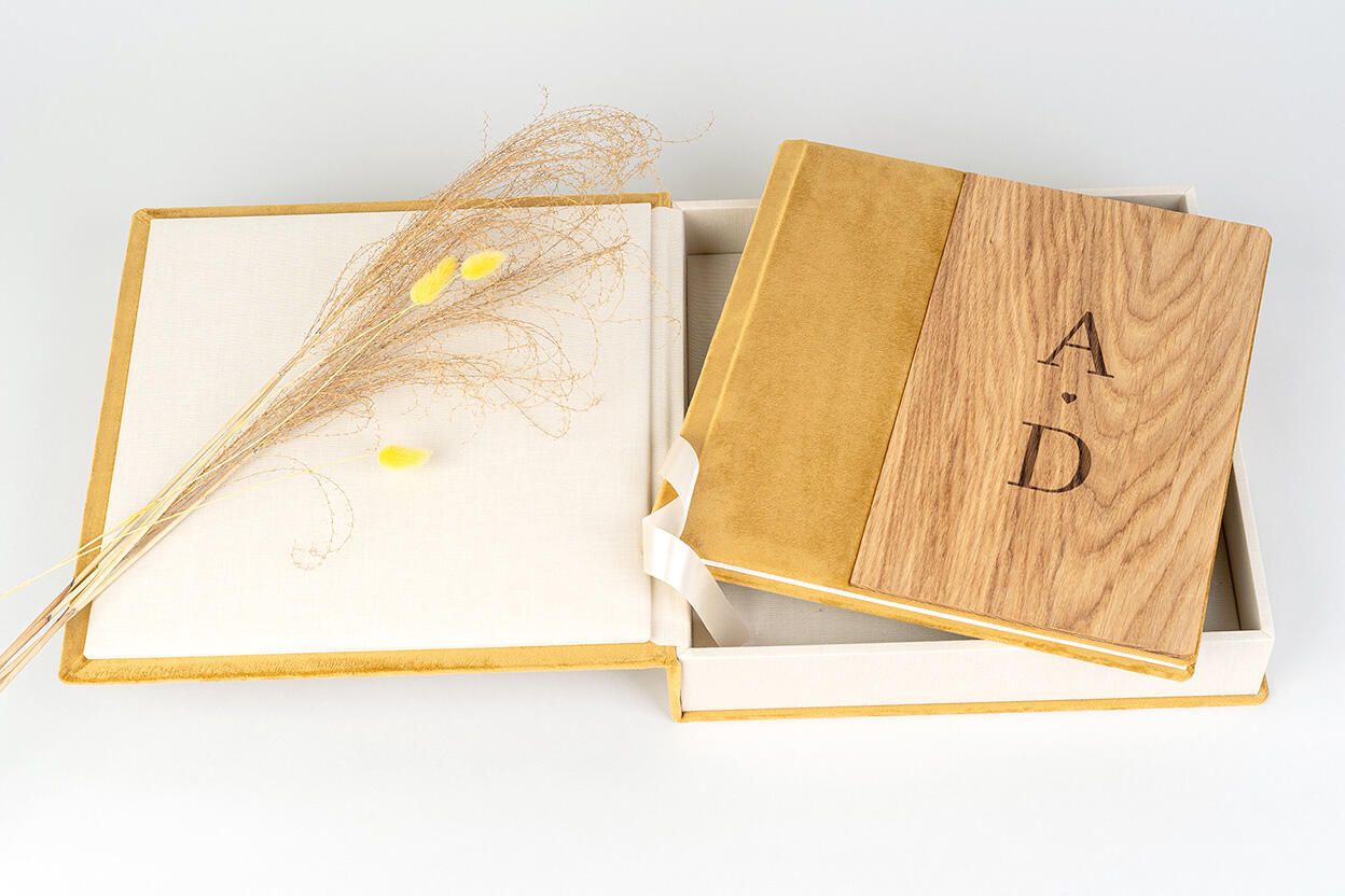 Wooden photo album with engraved initials A and D in an elegant gold-trimmed white keepsake box with dried flowers.