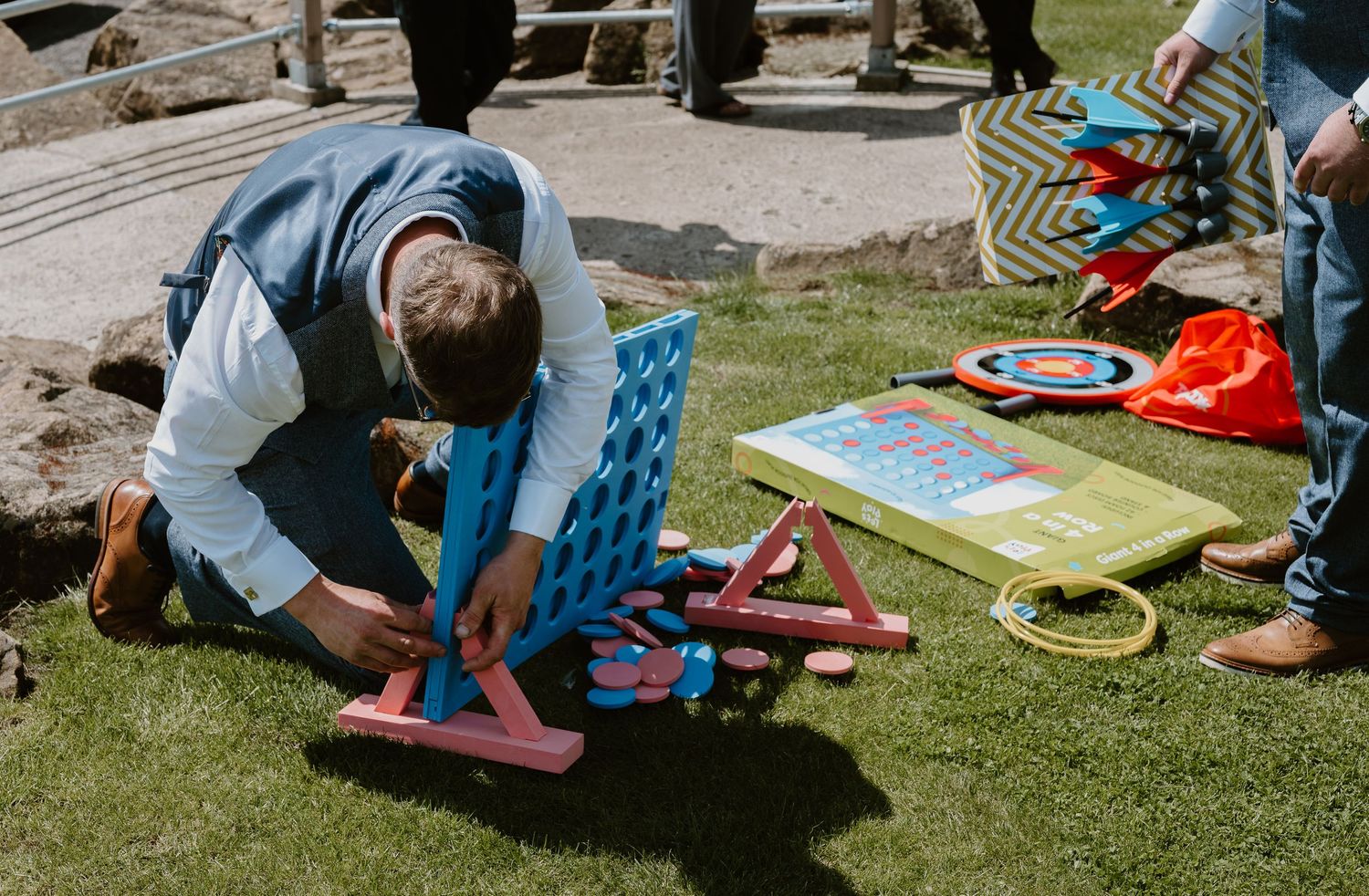 Man setting up a Connect Four game on grass at an outdoor event with archery targets and lawn games.