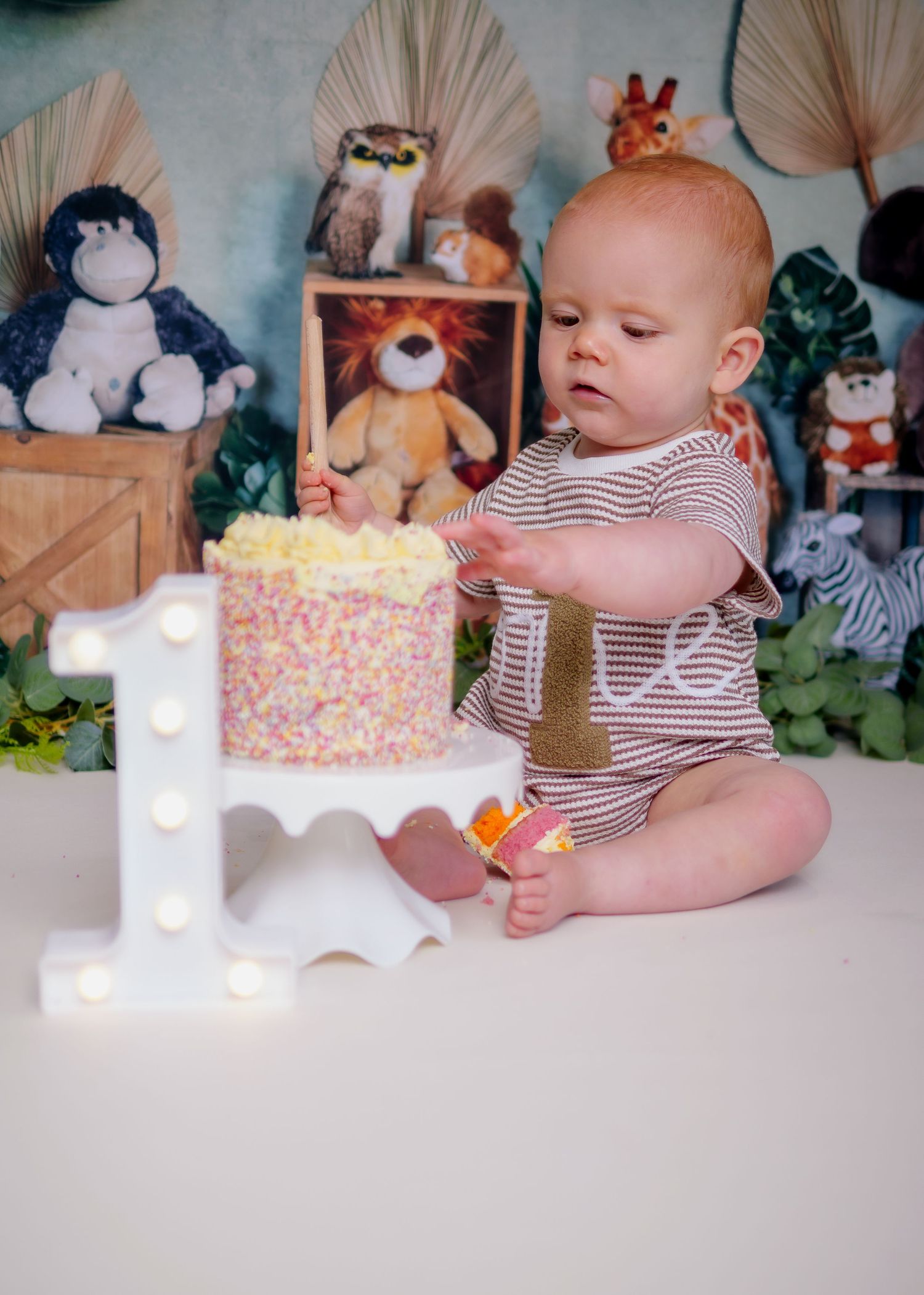 First birthday celebration setup with cake and decorations against a neutral backdrop. Cake Smash