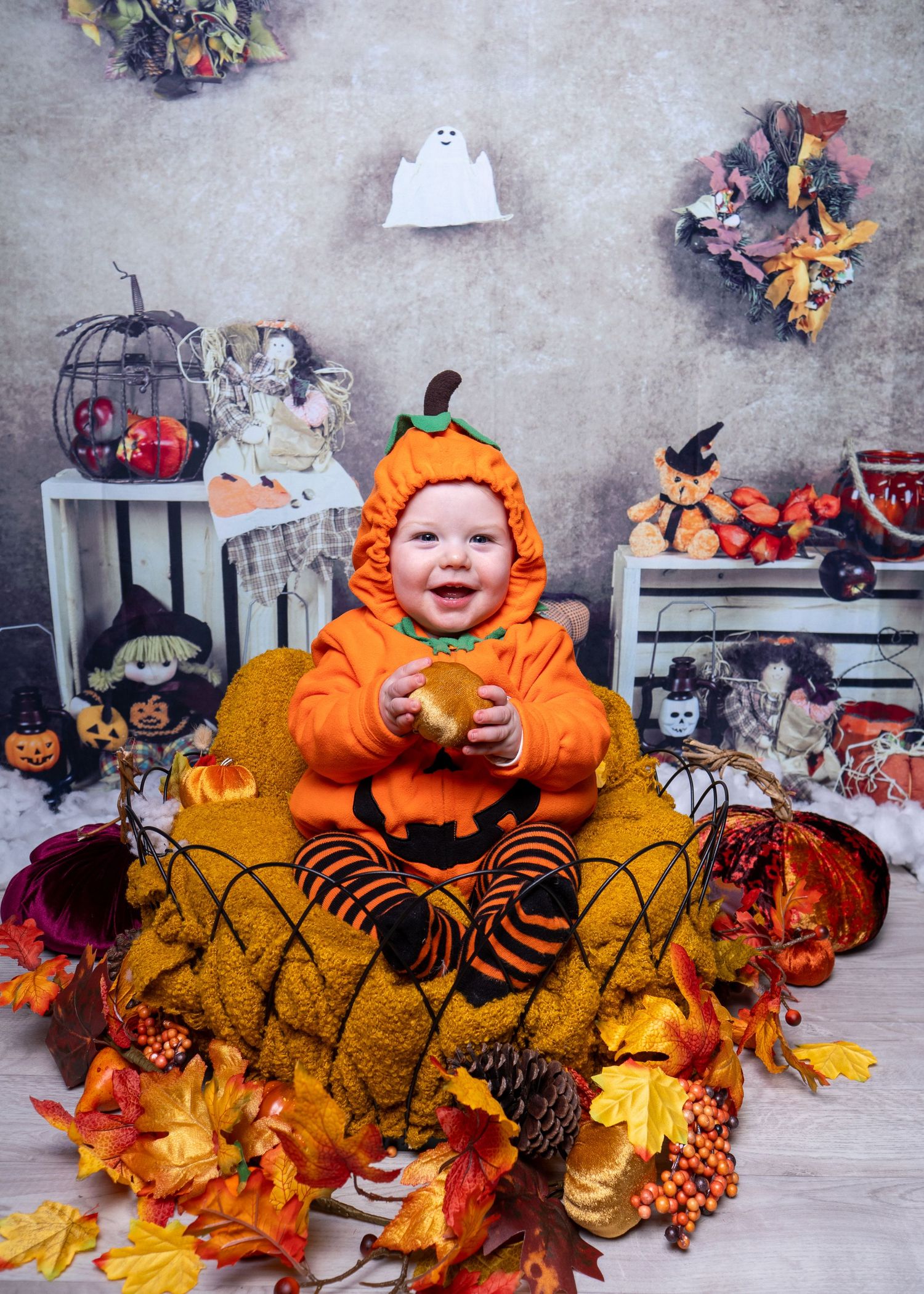Baby in orange pumpkin costume surrounded by Halloween decorations and fall leaves. Halloween Mini Session