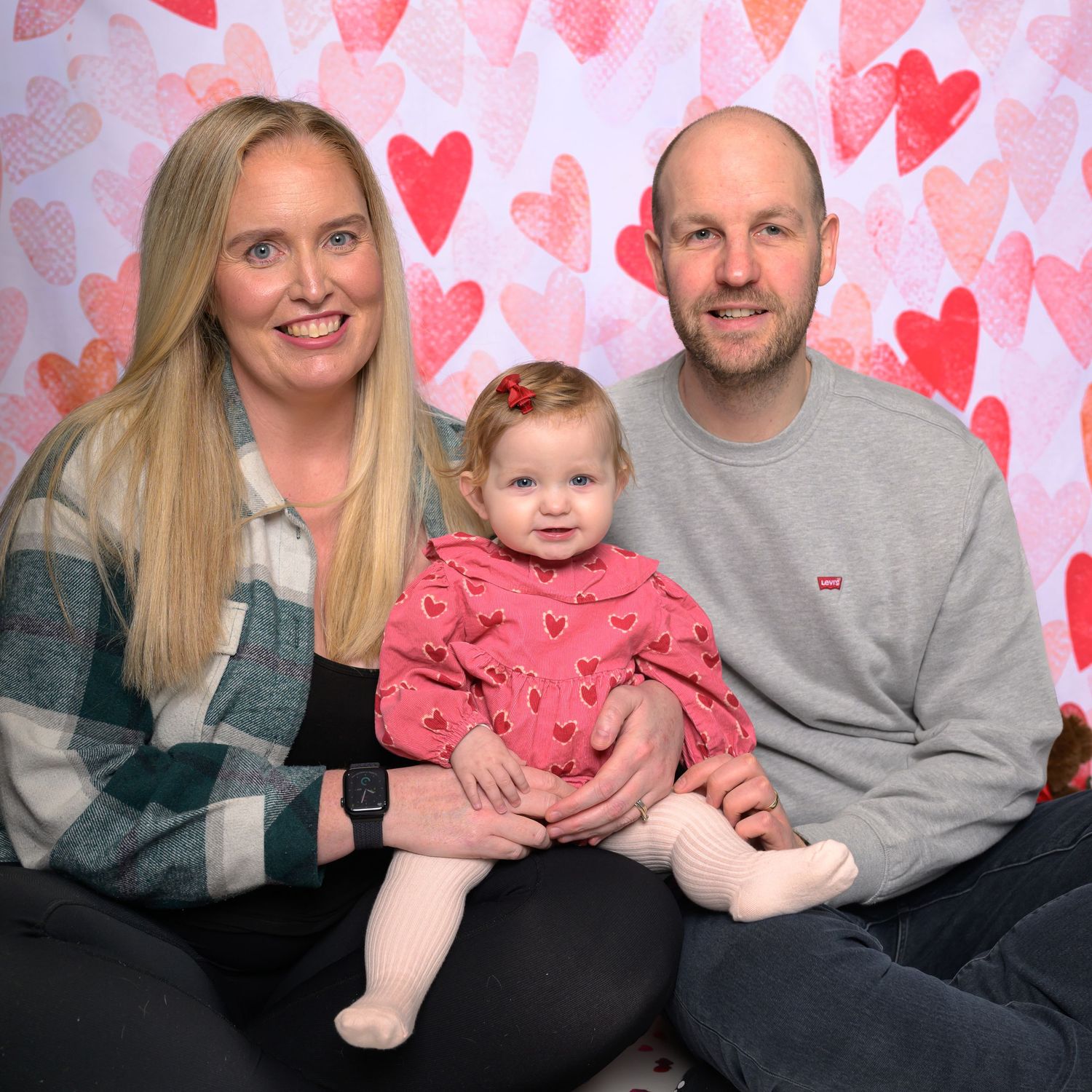 Family poses together against heart-patterned background in series of Valentine's Day themed photos.