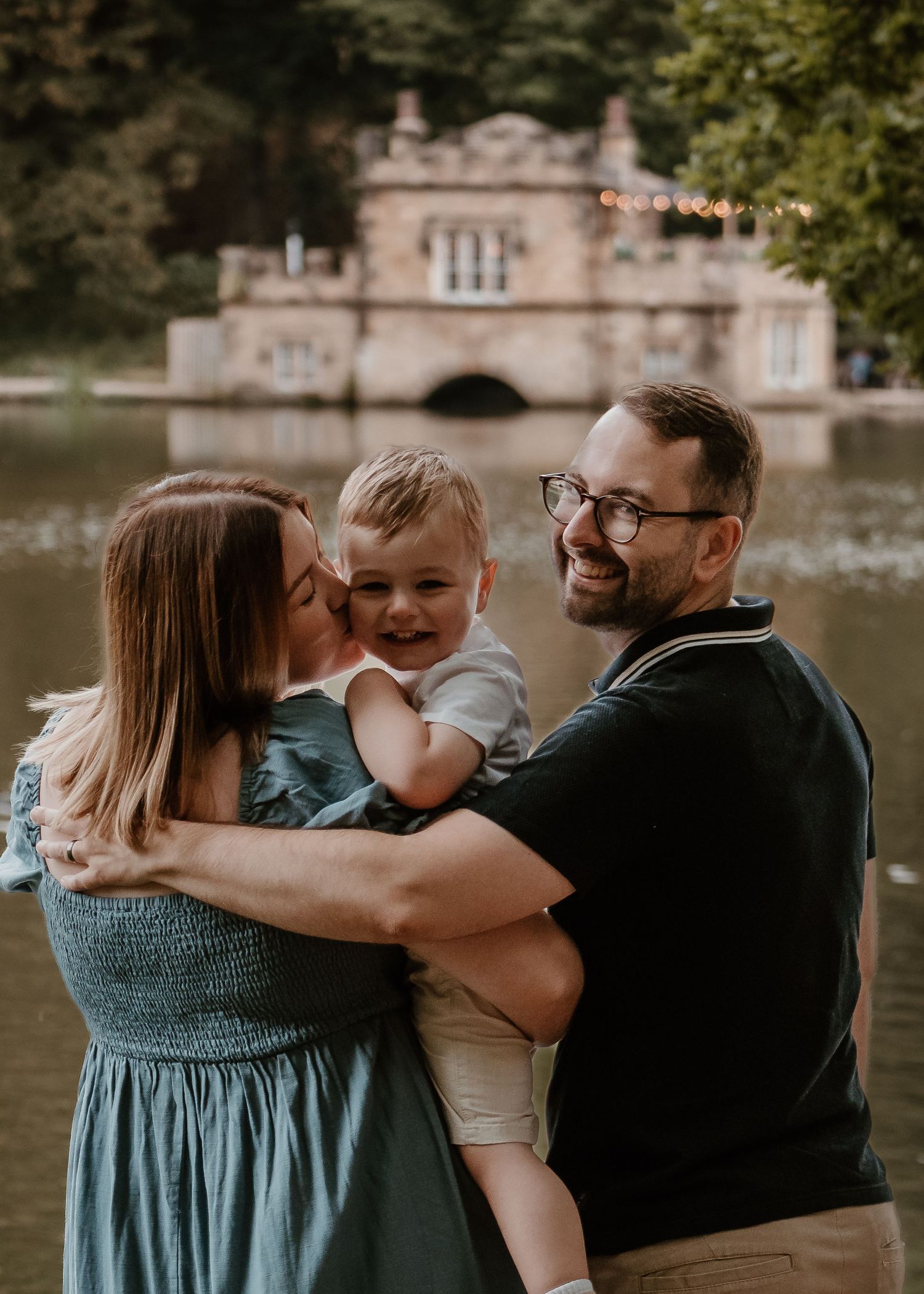 Family Photoshoot - Newmillerdam - Family sharing intimate moment by lakeside with historic building in background.
