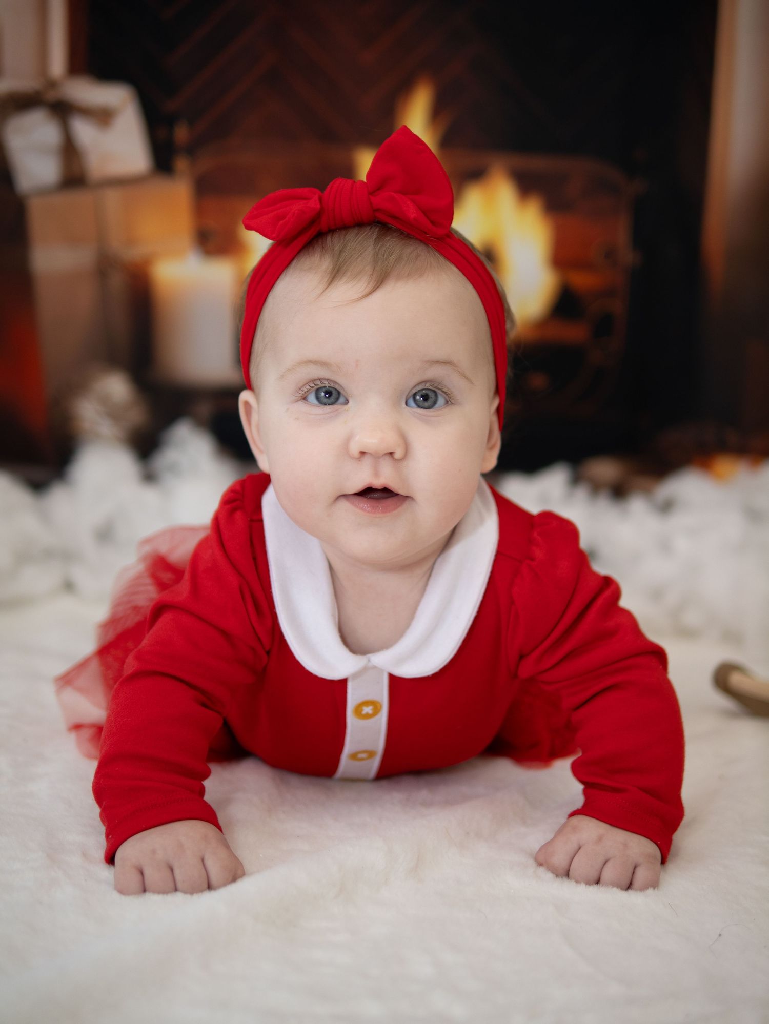 Baby in red Santa outfit crawling on white fluffy rug. Christmas Mini Session