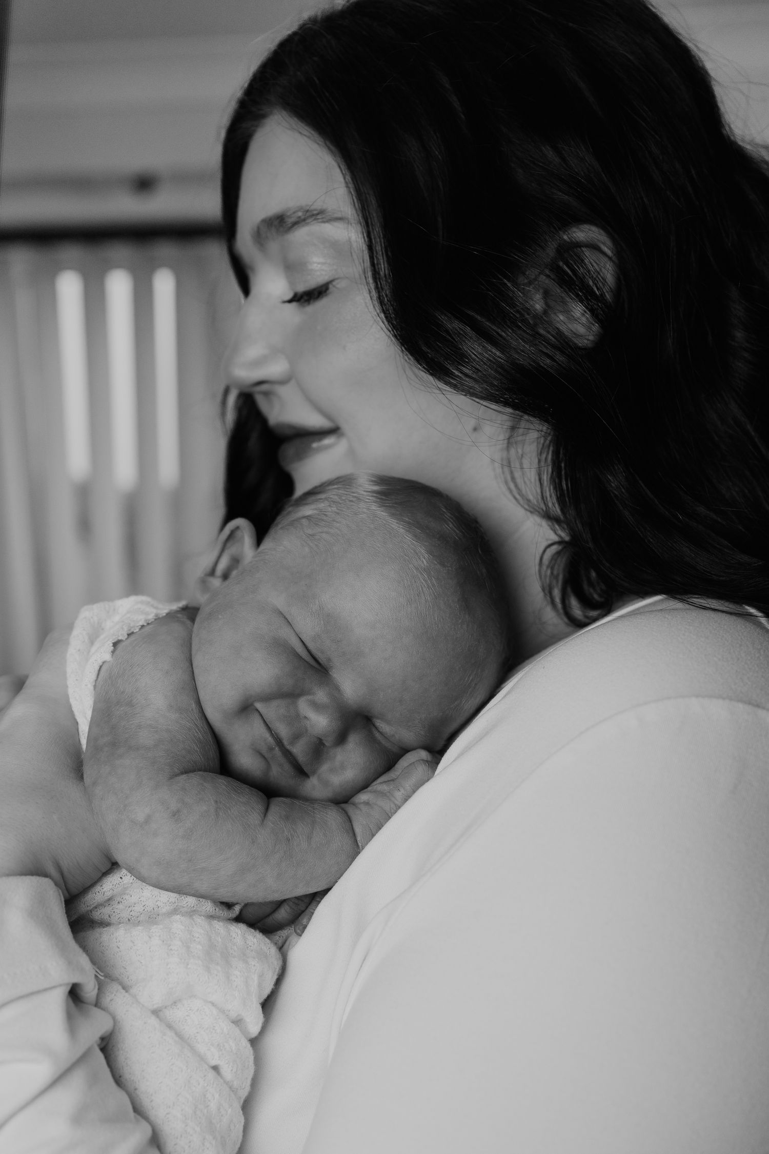 Black and white photo of a smiling mother tenderly holding her sleeping newborn baby close to her chest.