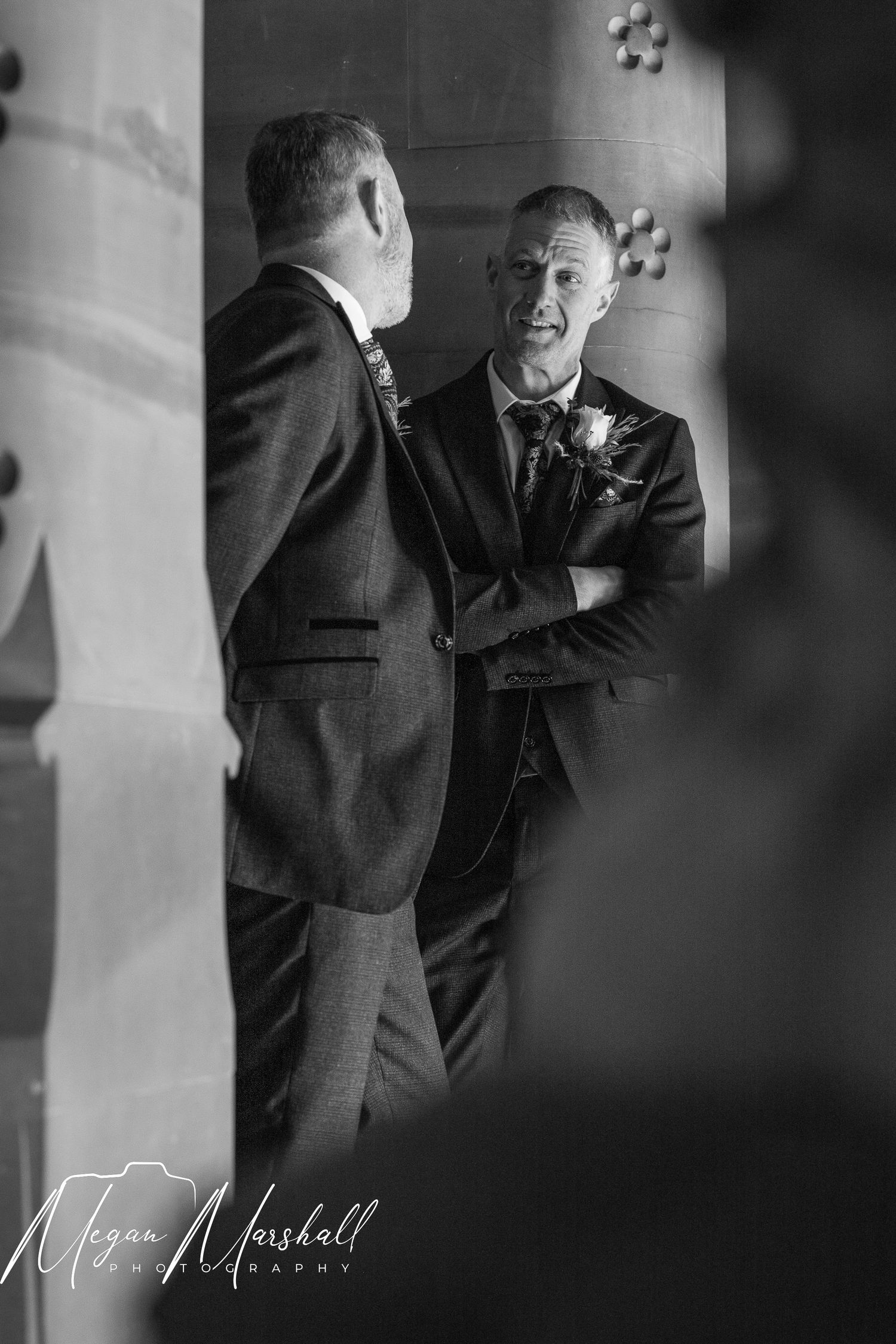 Black and white wedding photo of two grooms in suits sharing a moment before the ceremony.