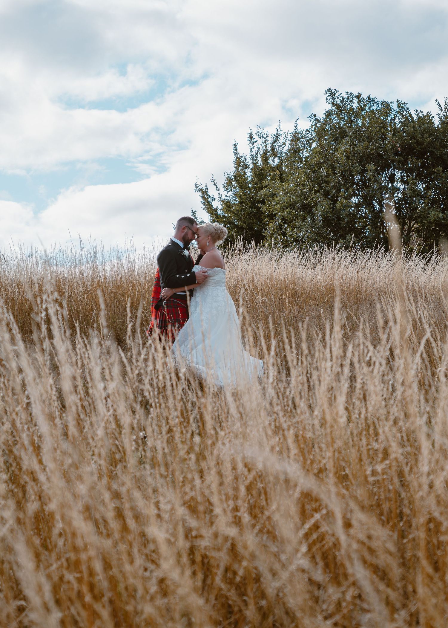 Waterton Park Hotel - Wedding couple walking through tall golden grass in a scenic outdoor field.