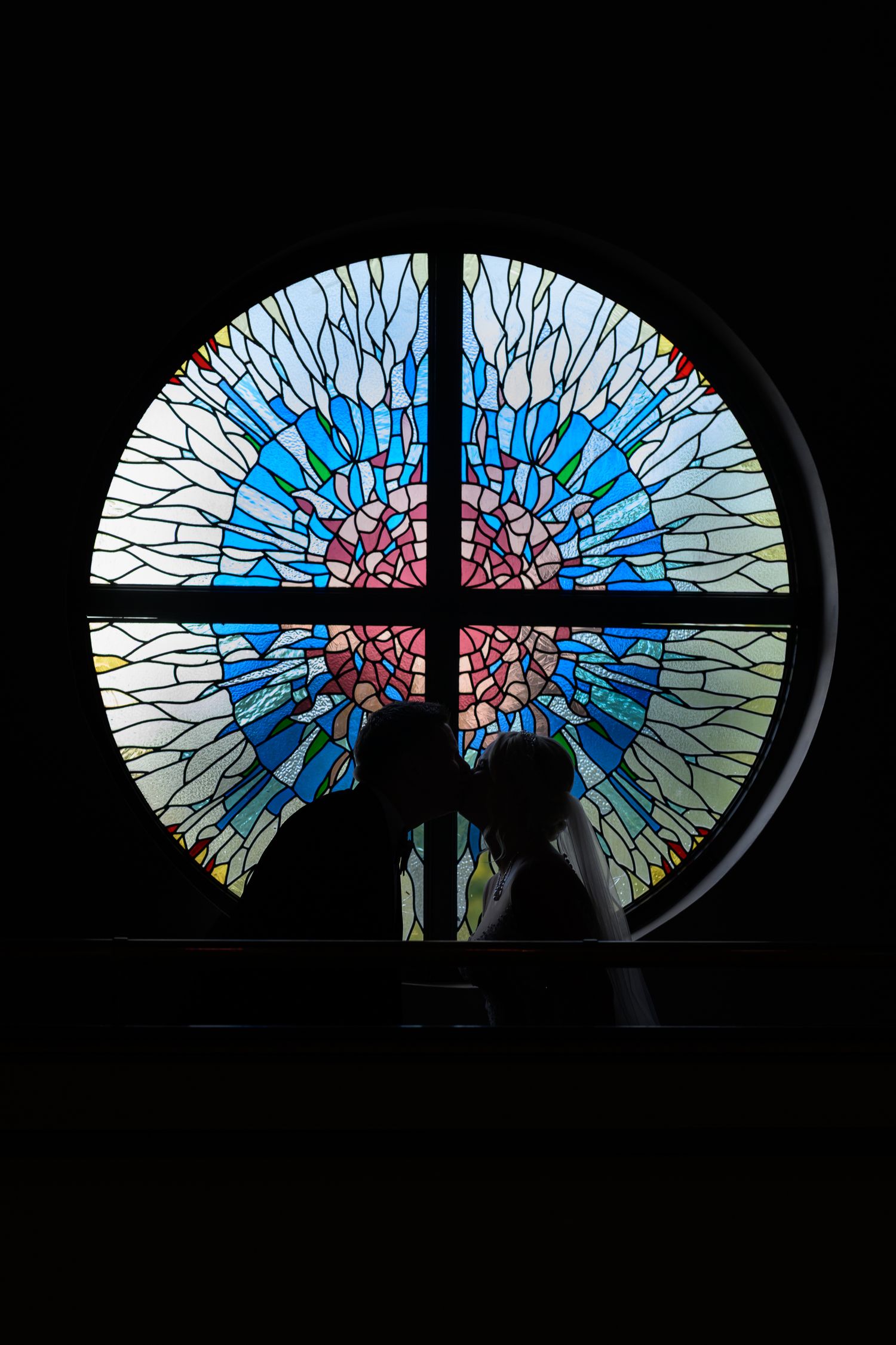 At Burntwood Court Hotel. A silhouetted figure stands before a colorful stained glass window with blue and pink mosaic patterns.