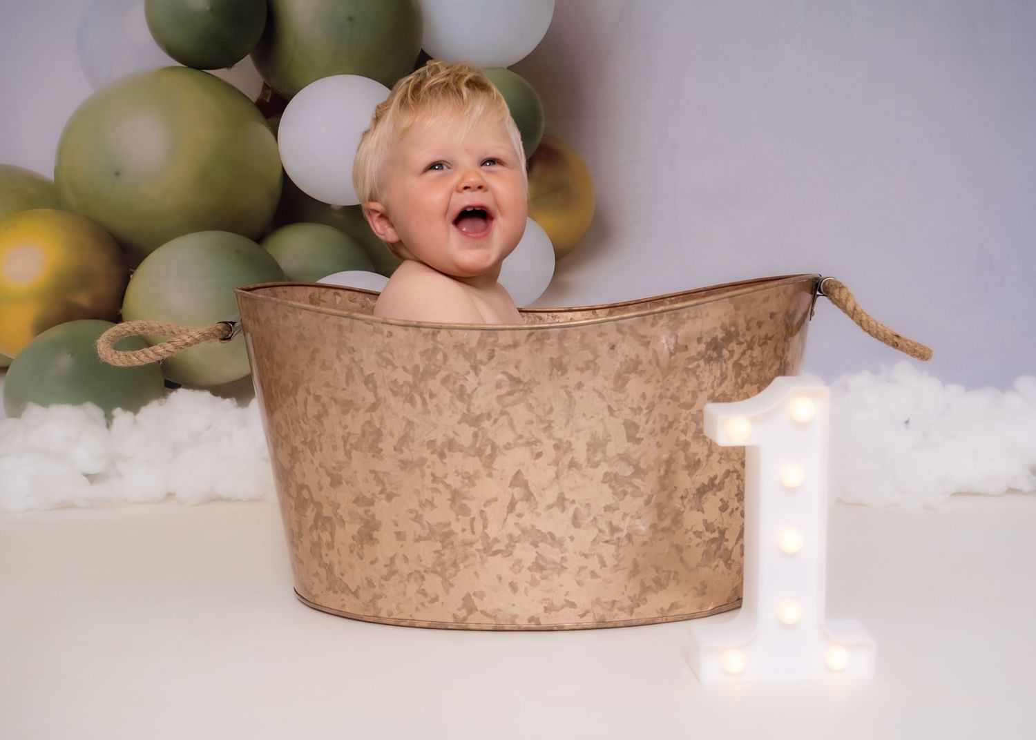 Birthday setup featuring rustic metal tub and green balloon arch with number one light. Cake Smash Photoshoot