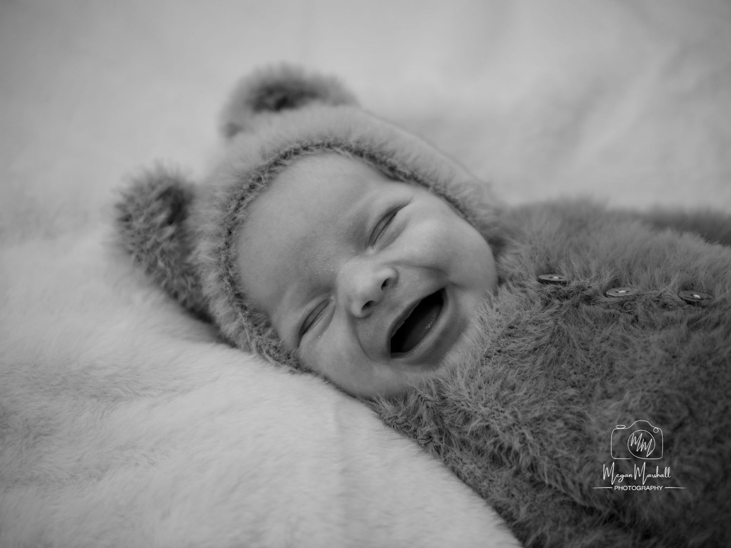 Black and white portrait of baby wearing fuzzy bear hat while smiling. Newborn photoshoot in Penistone