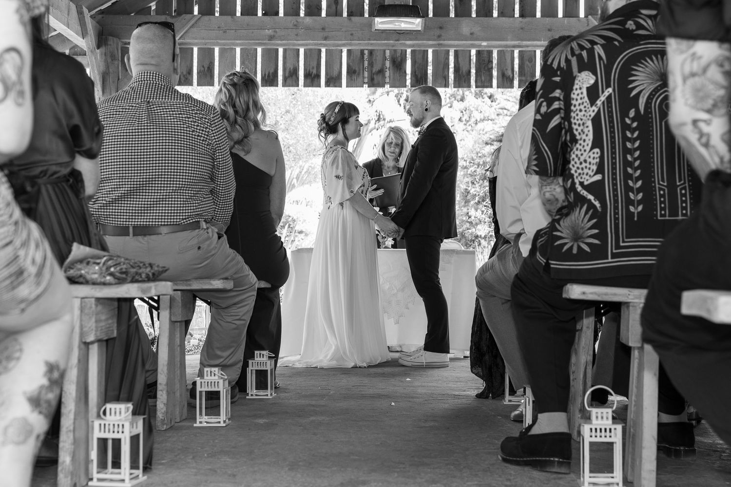 Black and white wedding ceremony photo of bride and groom exchanging vows at altar with guests seated in pews.