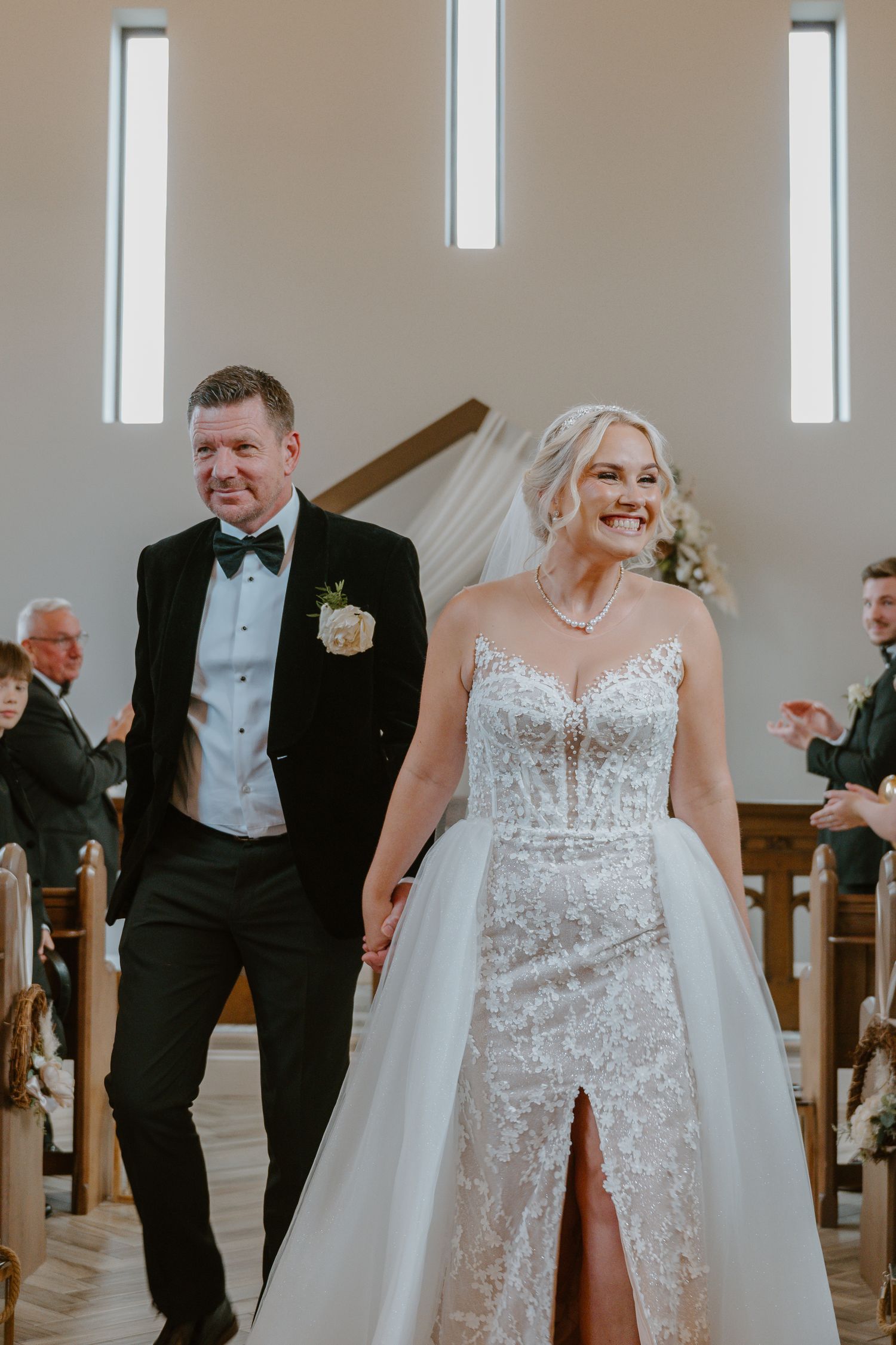 Burntwood Court Hotel. A joyful wedding party walks down the aisle in a bright church with the bride wearing a sparkly white dress.