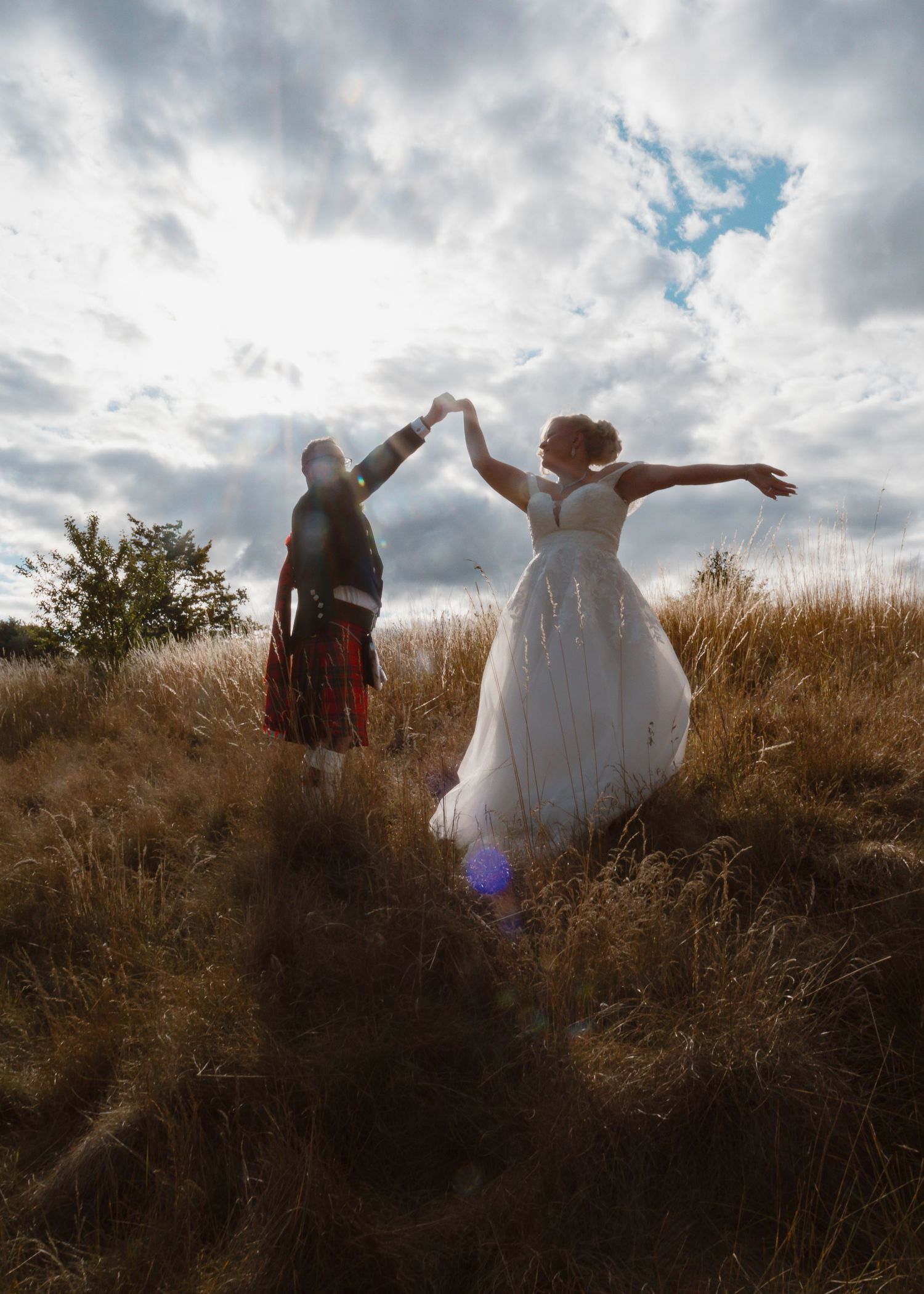 Waterton Park Hotel - A couple in wedding attire dance together on a hilltop against dramatic cloudy skies during golden hour.