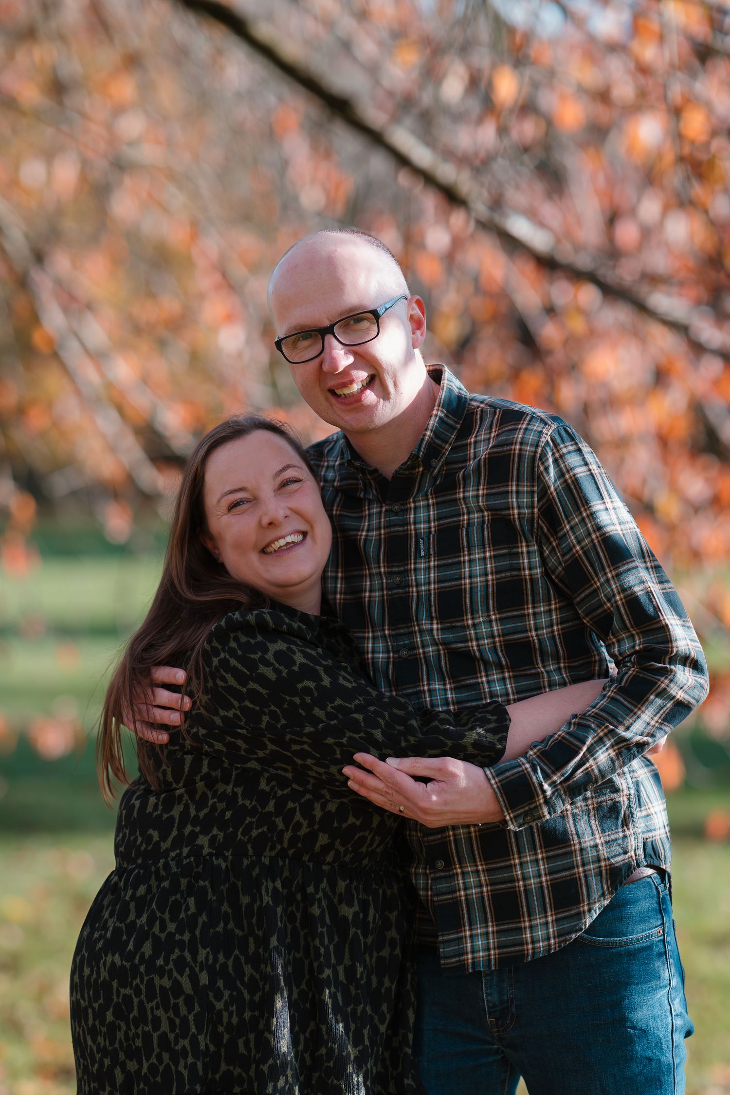 A couple shares joyful laughter together during an autumn photoshoot with orange leaves in the background.