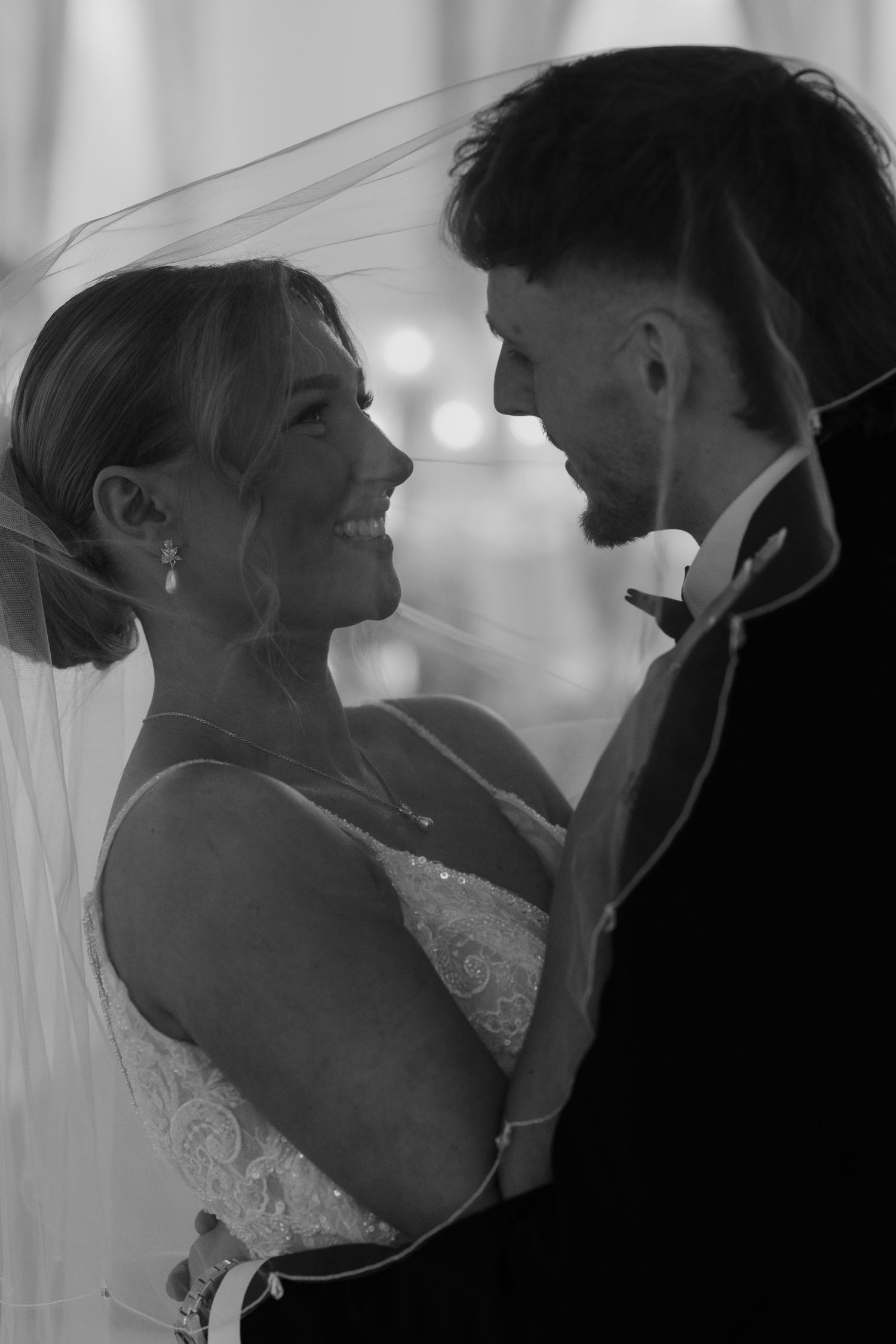 Black and white wedding photo of smiling bride in veil and groom sharing an intimate moment together.
