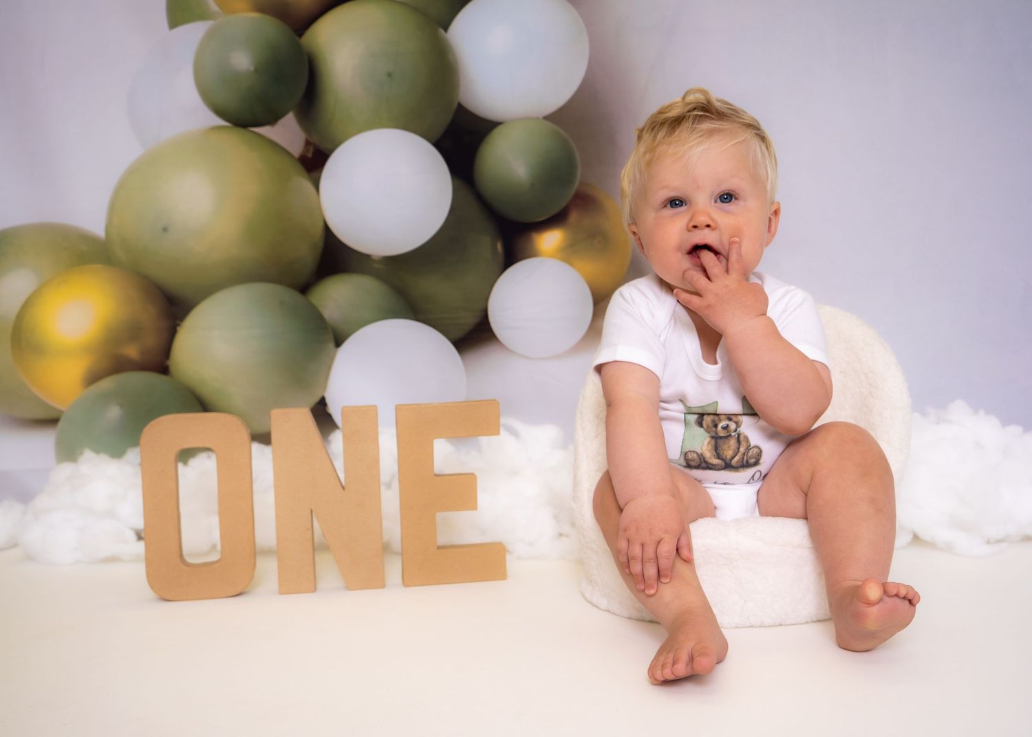 Birthday setup with wooden 'ONE' letters and green balloon garland. Cake Smash Photoshoot