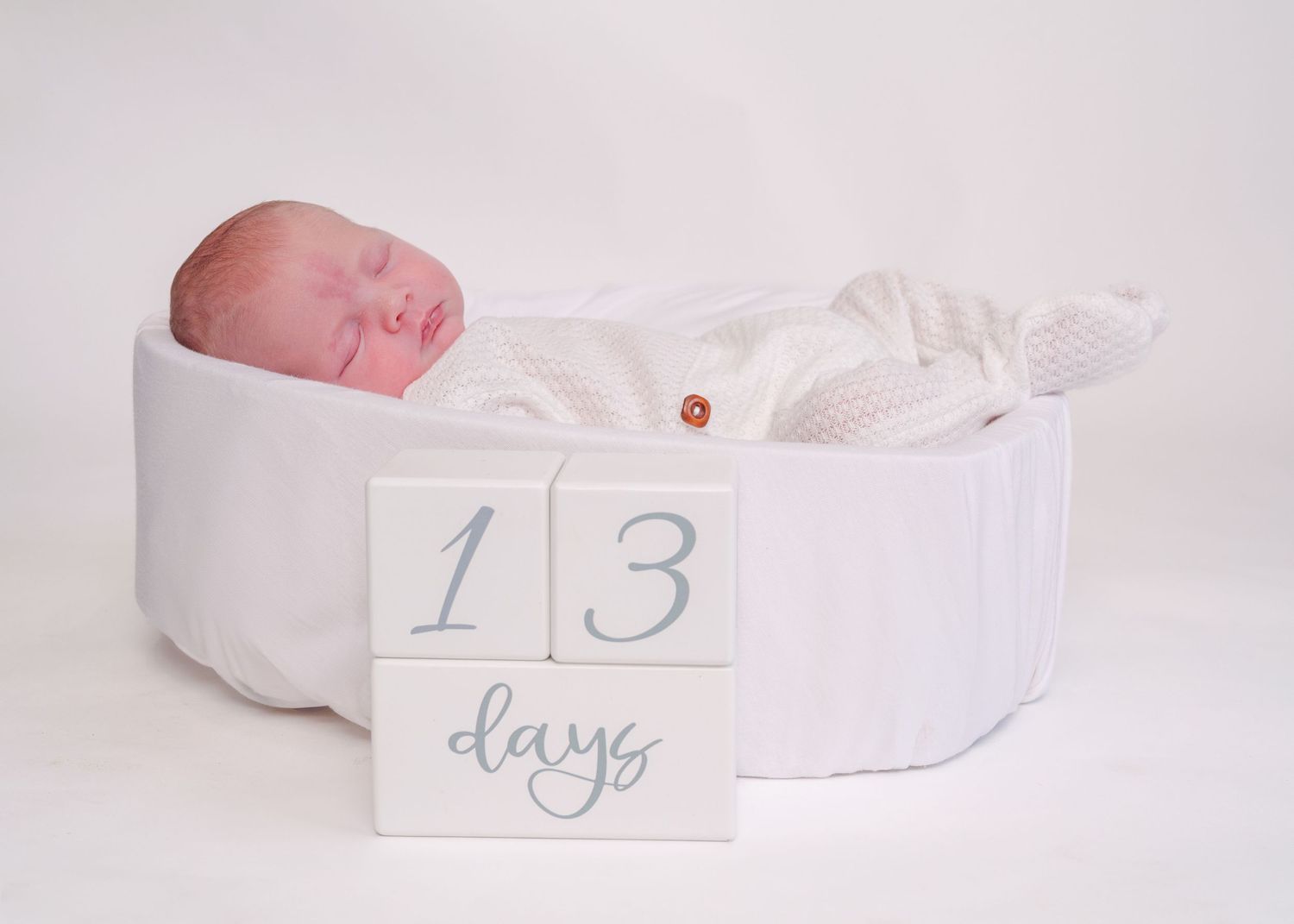 Newborn milestone photography with white fabric and number cards.