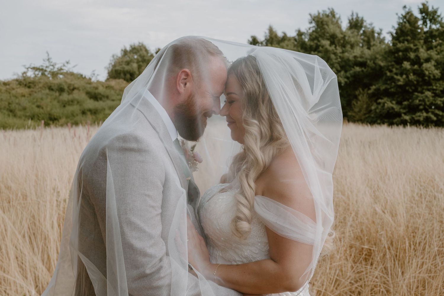 Bride and groom sharing an intimate moment under a wedding veil in a golden wheat field.