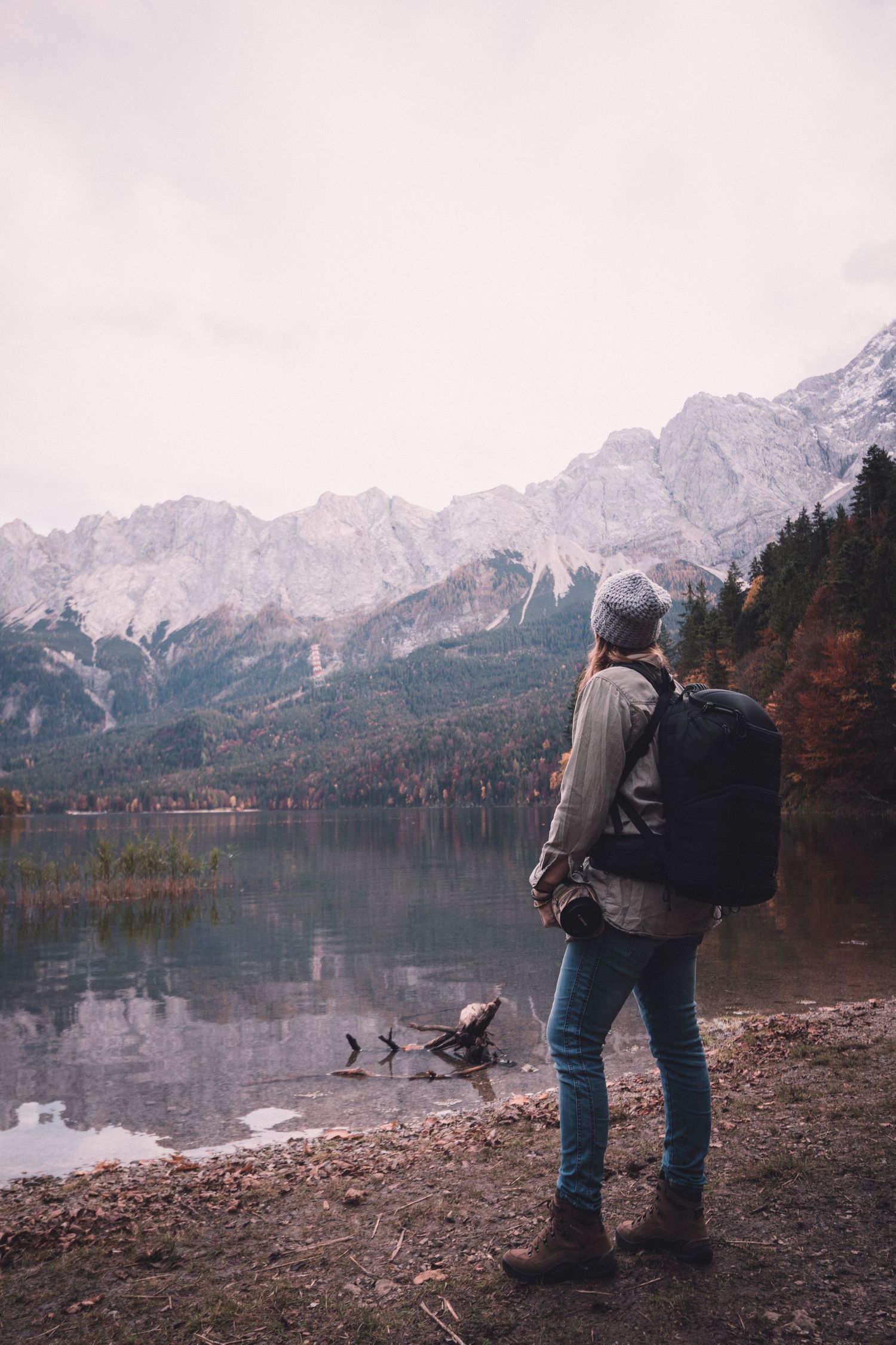 Marjolein with backpack standing by alpine lake with snow-capped mountain reflections in autumn.