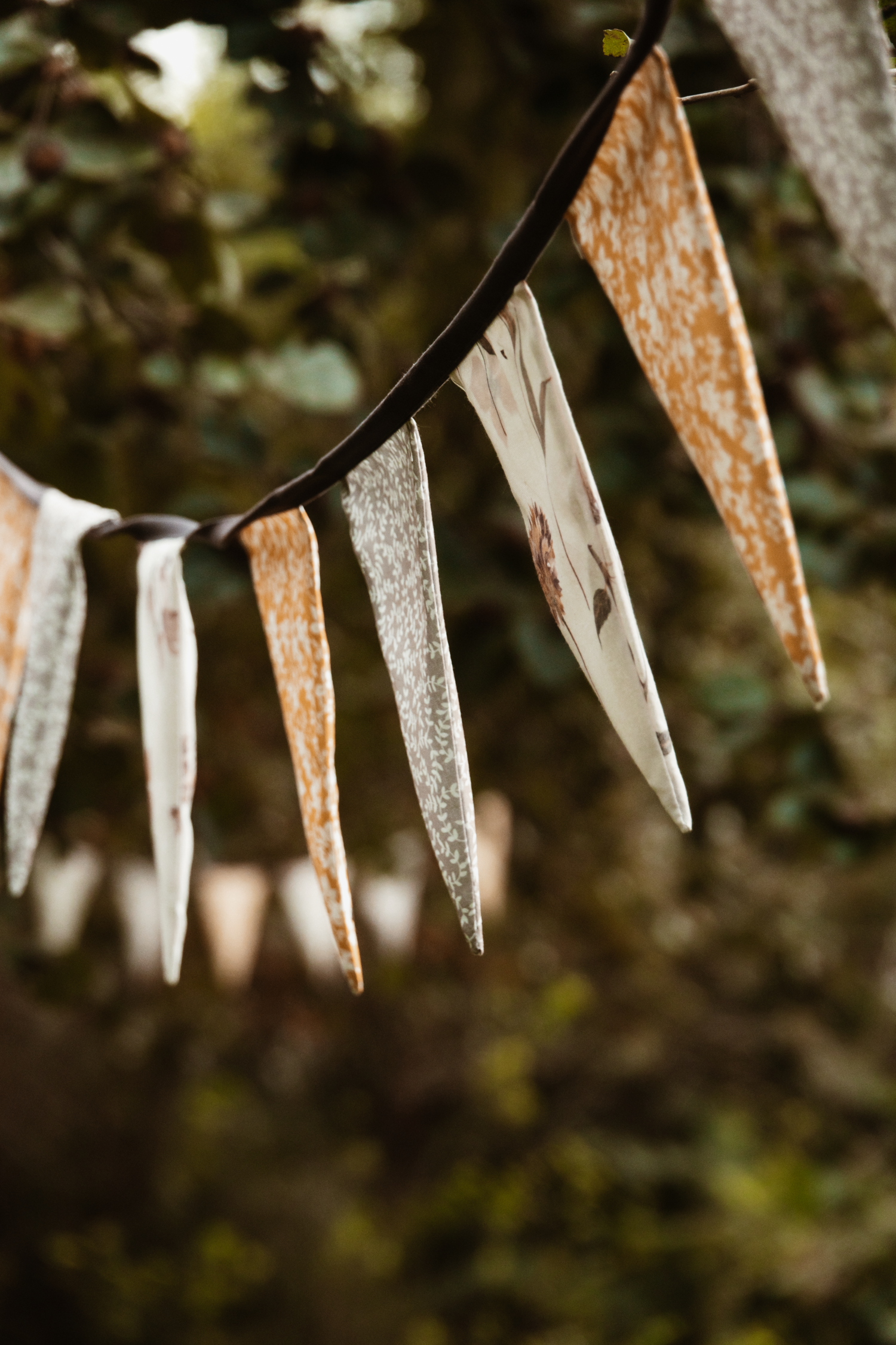 Rustic fabric bunting flags hanging on a string outdoors with green foliage background.